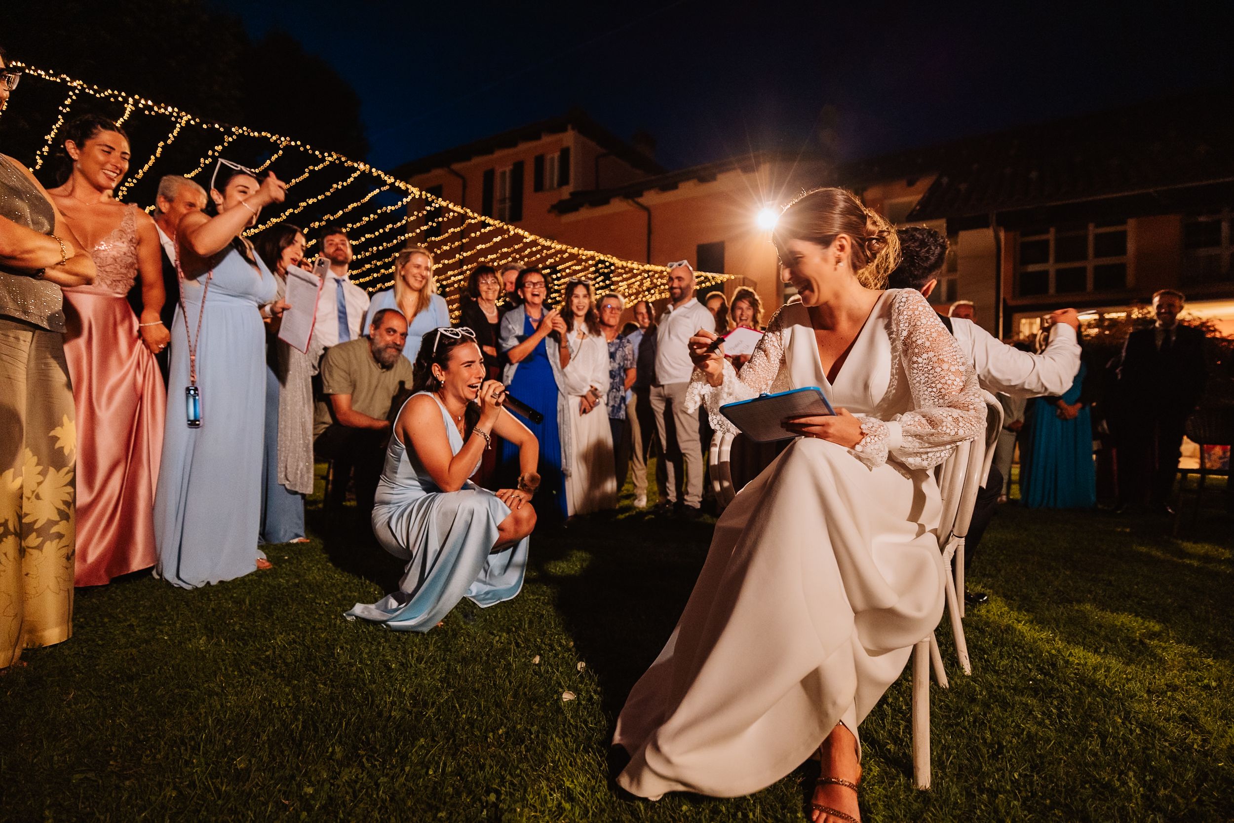 Wedding guests seated on a grassy lawn for an evening outdoor celebration with ambient lighting.