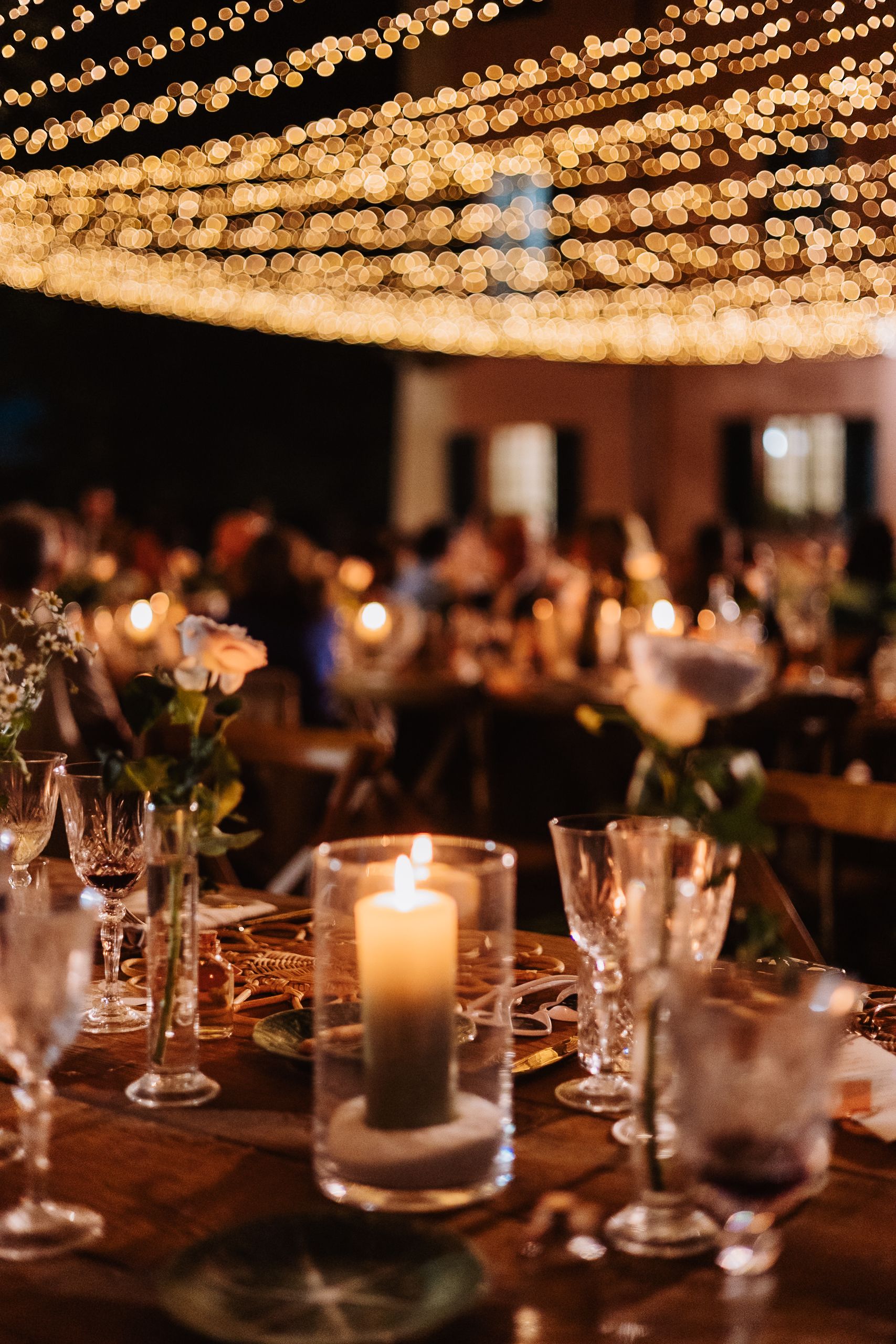 Rustic wedding reception table with glowing candles and string lights overhead creating a warm, romantic ambiance.