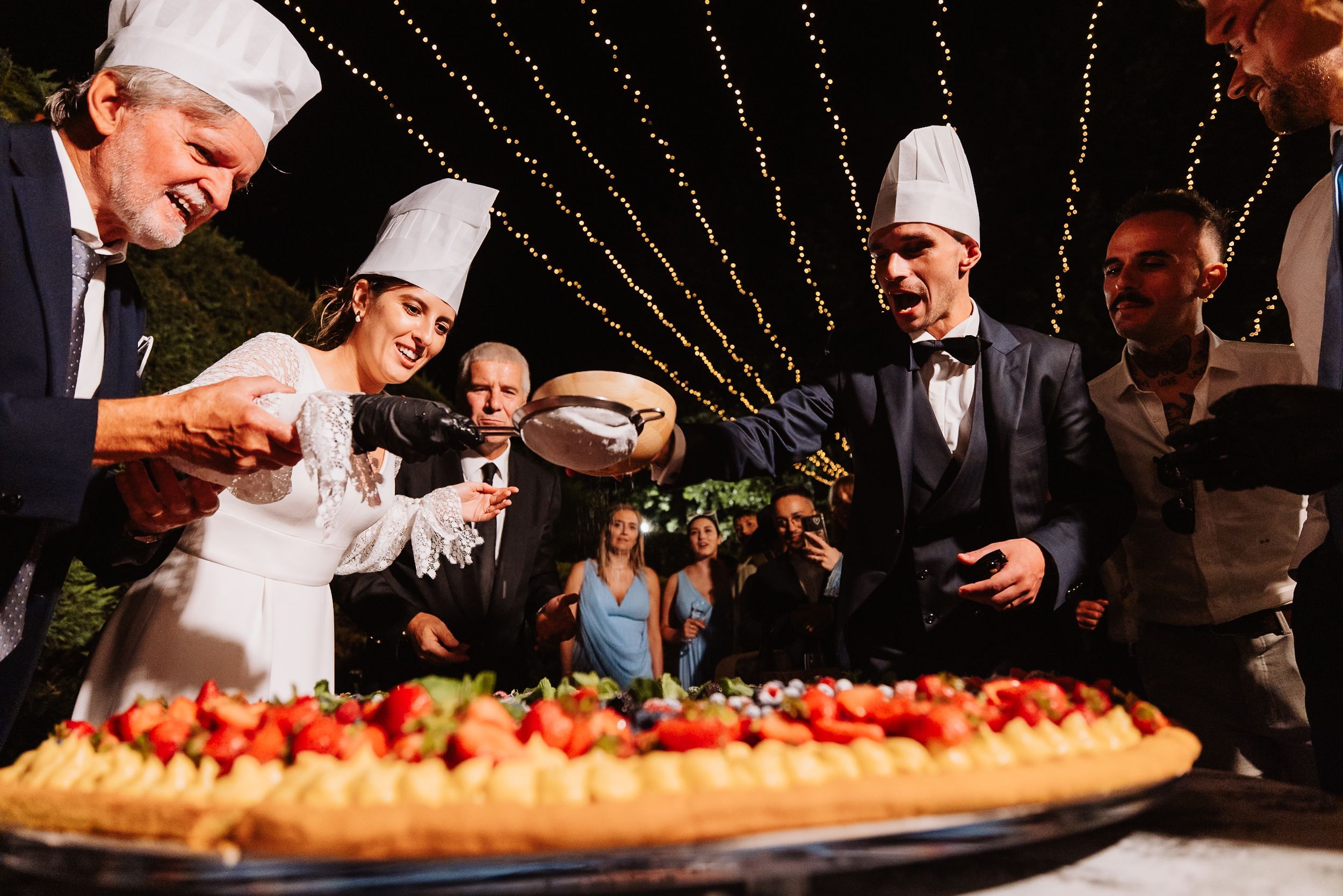 Chefs and guests gather around a long table displaying fresh ingredients and prepared dishes at a culinary event.