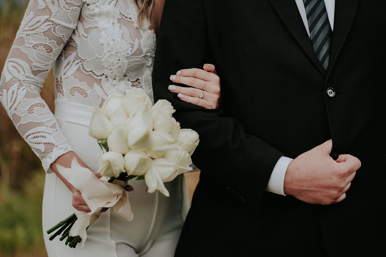 Close up view of wedding attire details showing white lace dress sleeve and dark suit jacket.