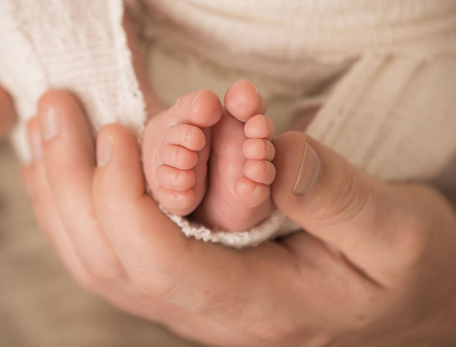 Close-up view of tiny baby feet and toes in soft, natural lighting against white fabric background.
