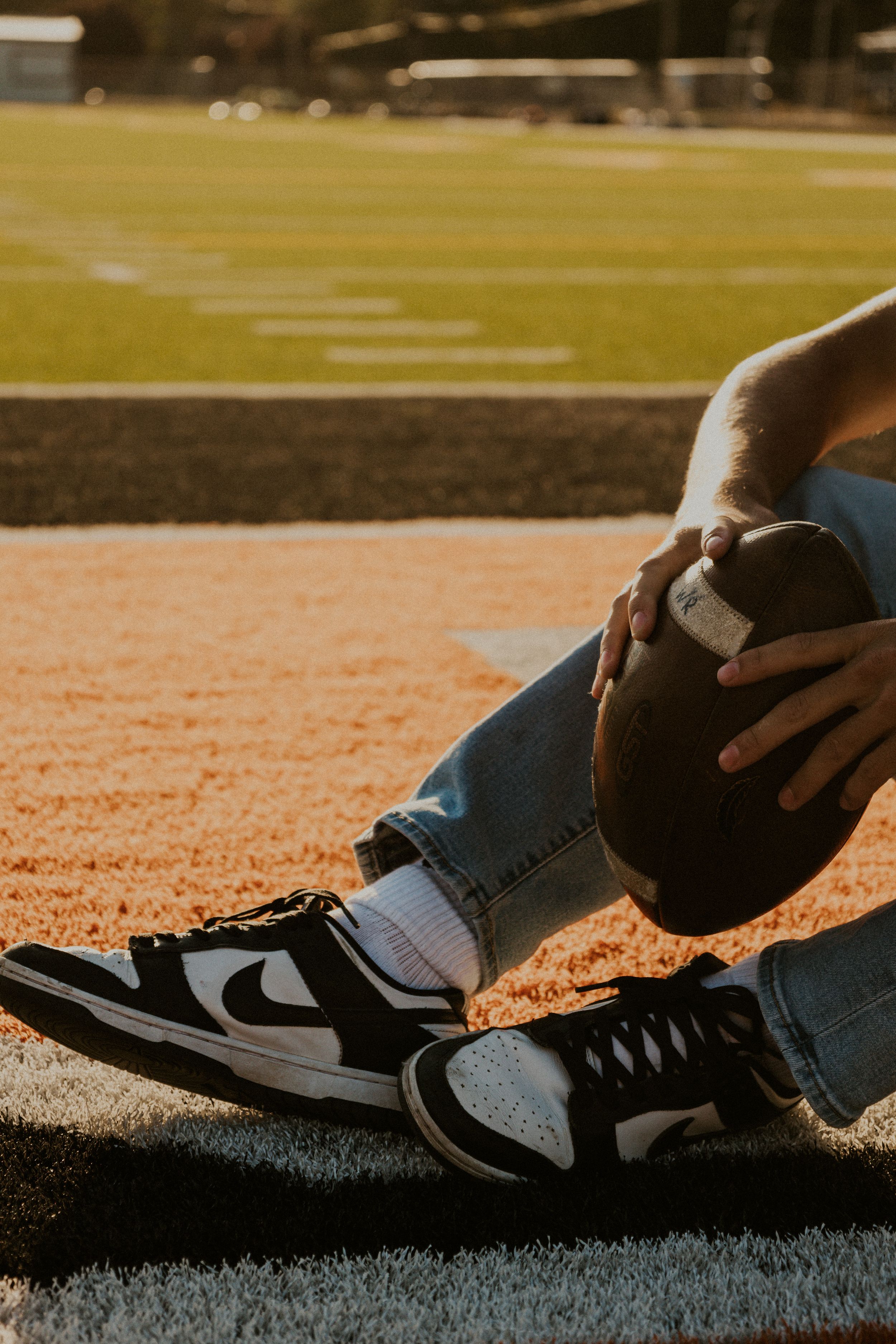 Close-up of black sneakers and jeans on football field during golden hour.