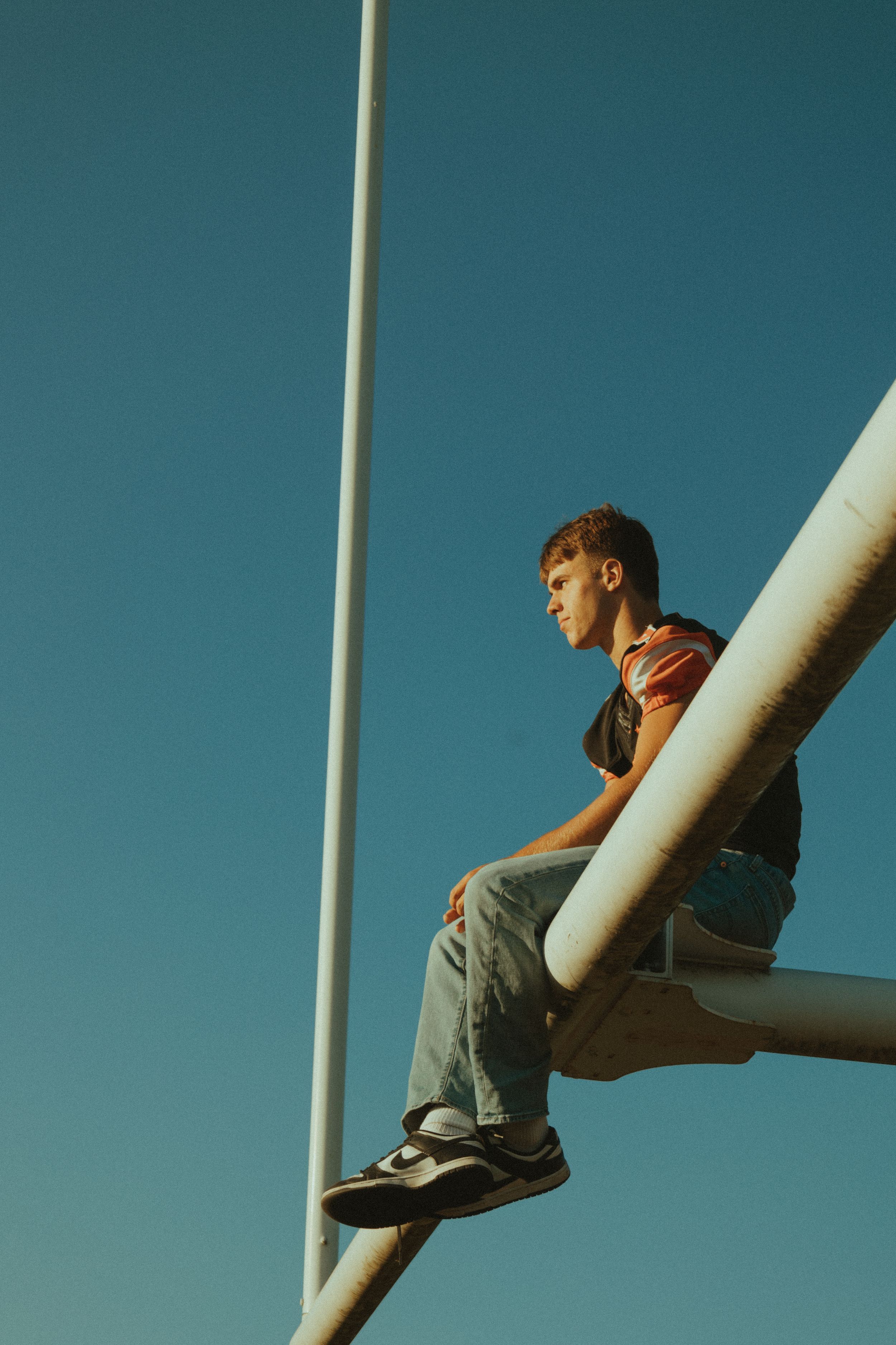 Person sitting on a white pole or beam against a vibrant blue sky background.