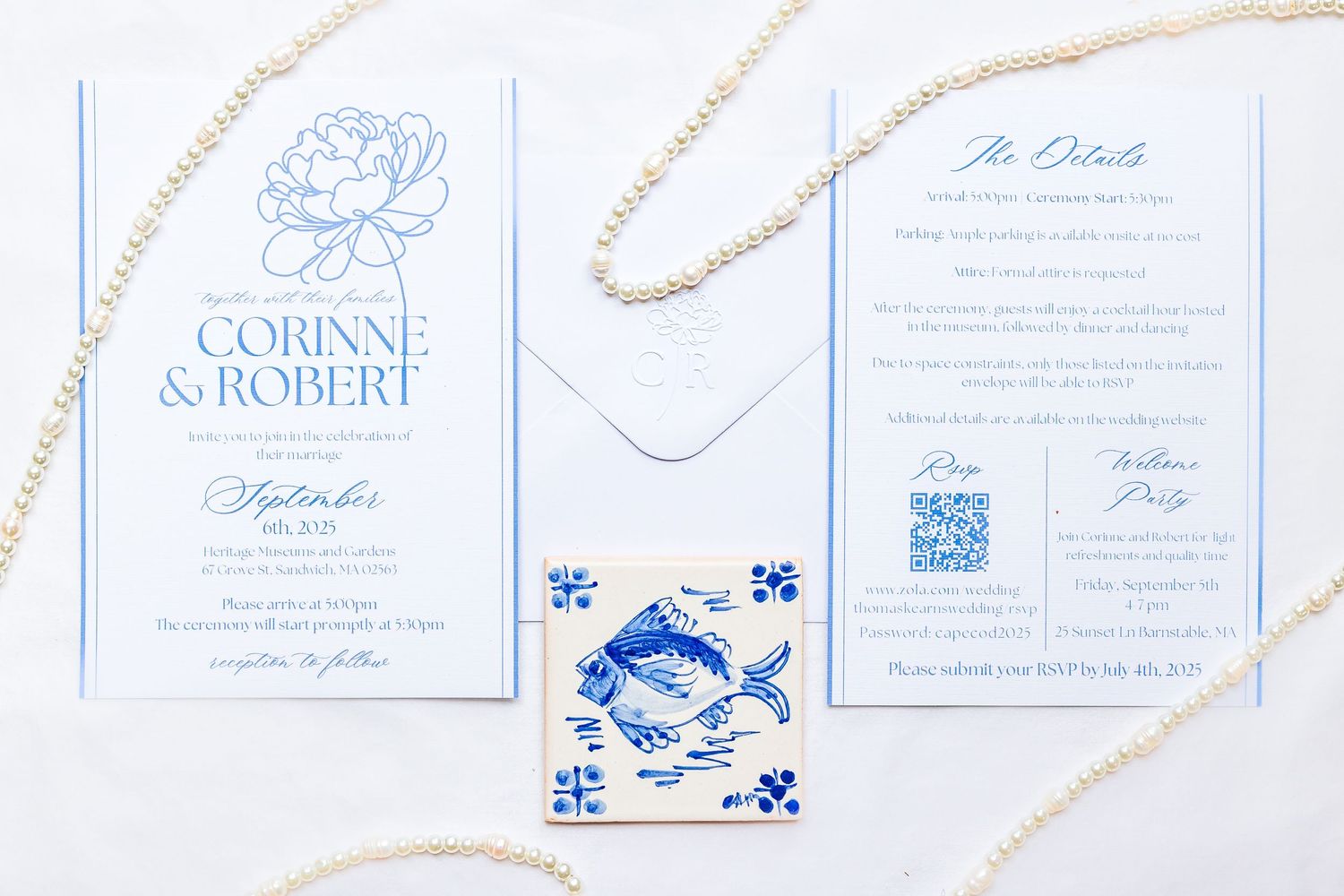 Light blue and white wedding invitation suite with floral details and decorative fish tile accent laid on white surface.