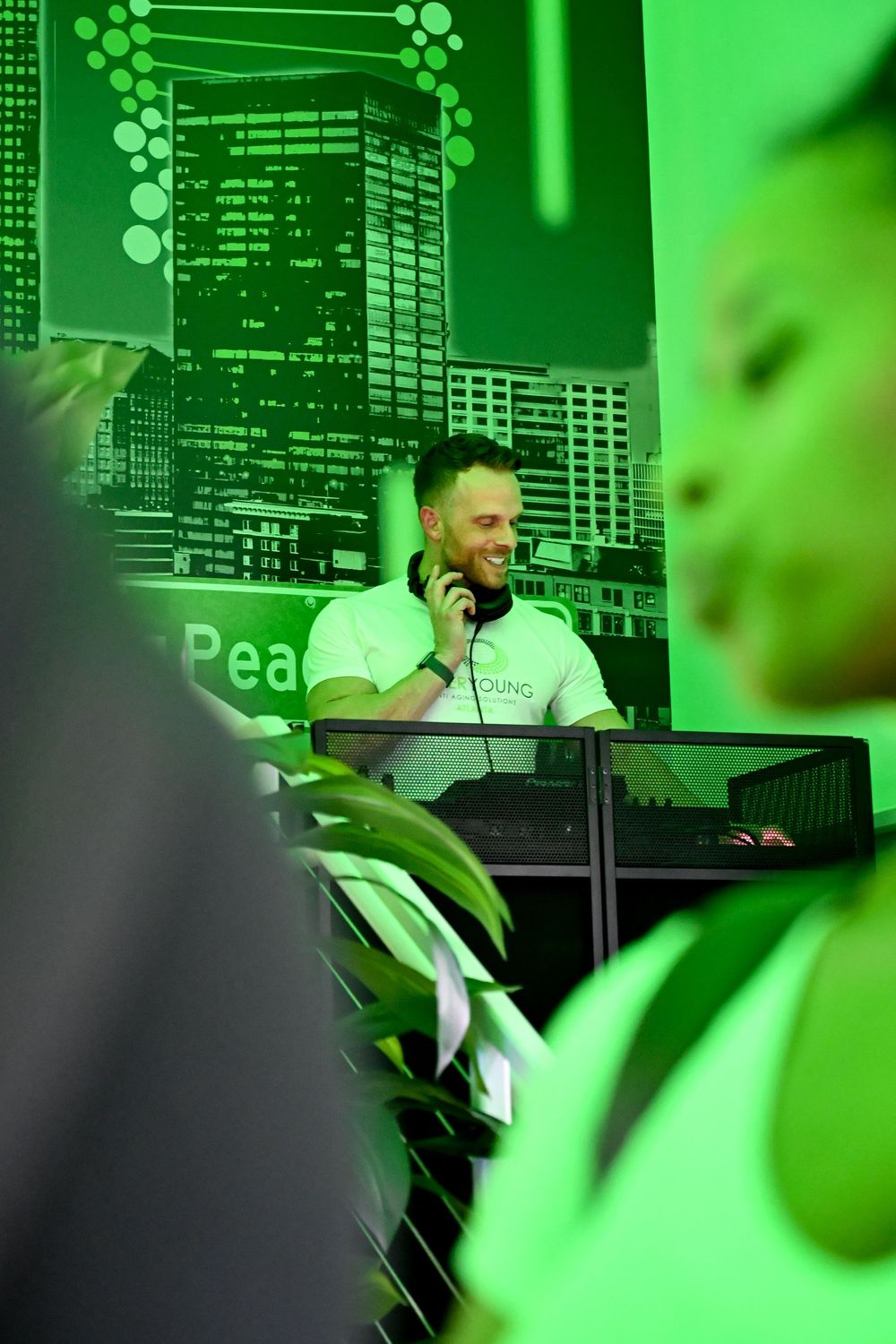 DJ performs at a nightclub with green lighting and digital displays in the background.