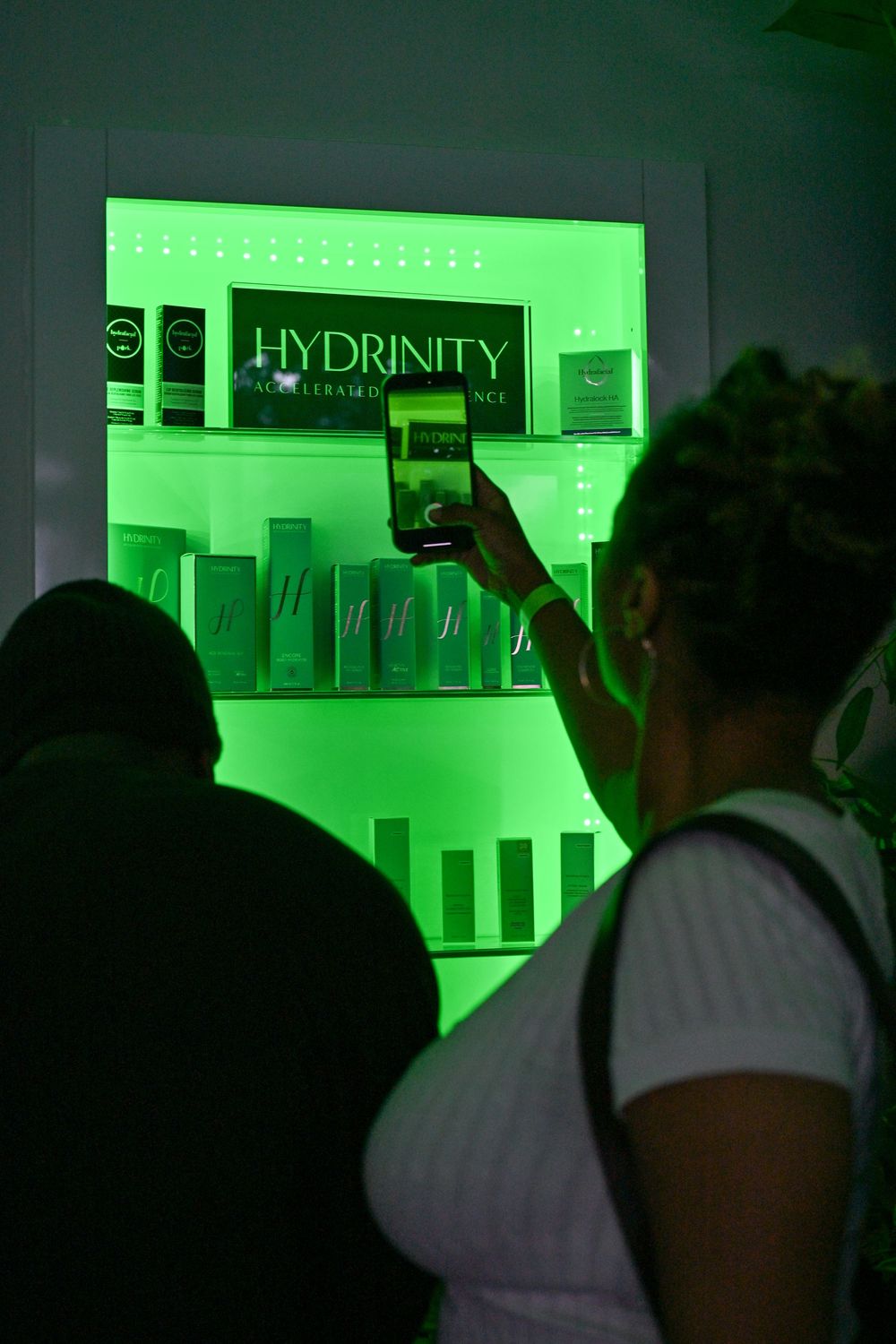 Product display shelf illuminated with green lighting showcasing Hydrinity skincare products in a retail setting.