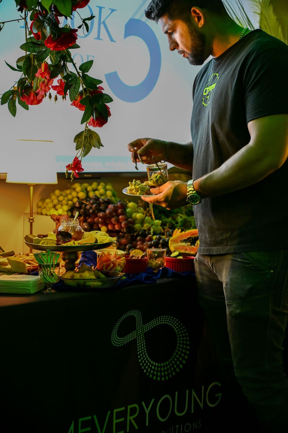People preparing fresh produce and ingredients at a food counter with fruits and vegetables.