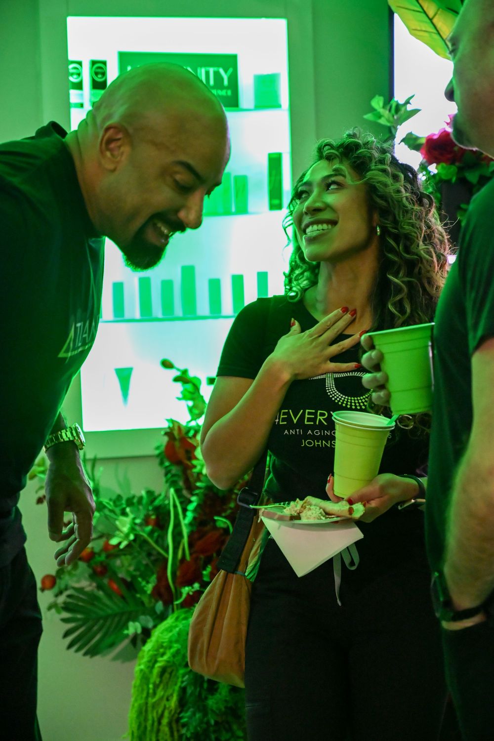People enjoying beverages in a green-lit modern space with tropical decor.