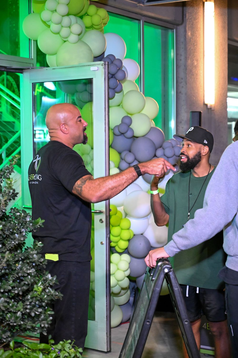 Event setup with green lighting and balloon arch decorations featuring grey and lime colored balloons.