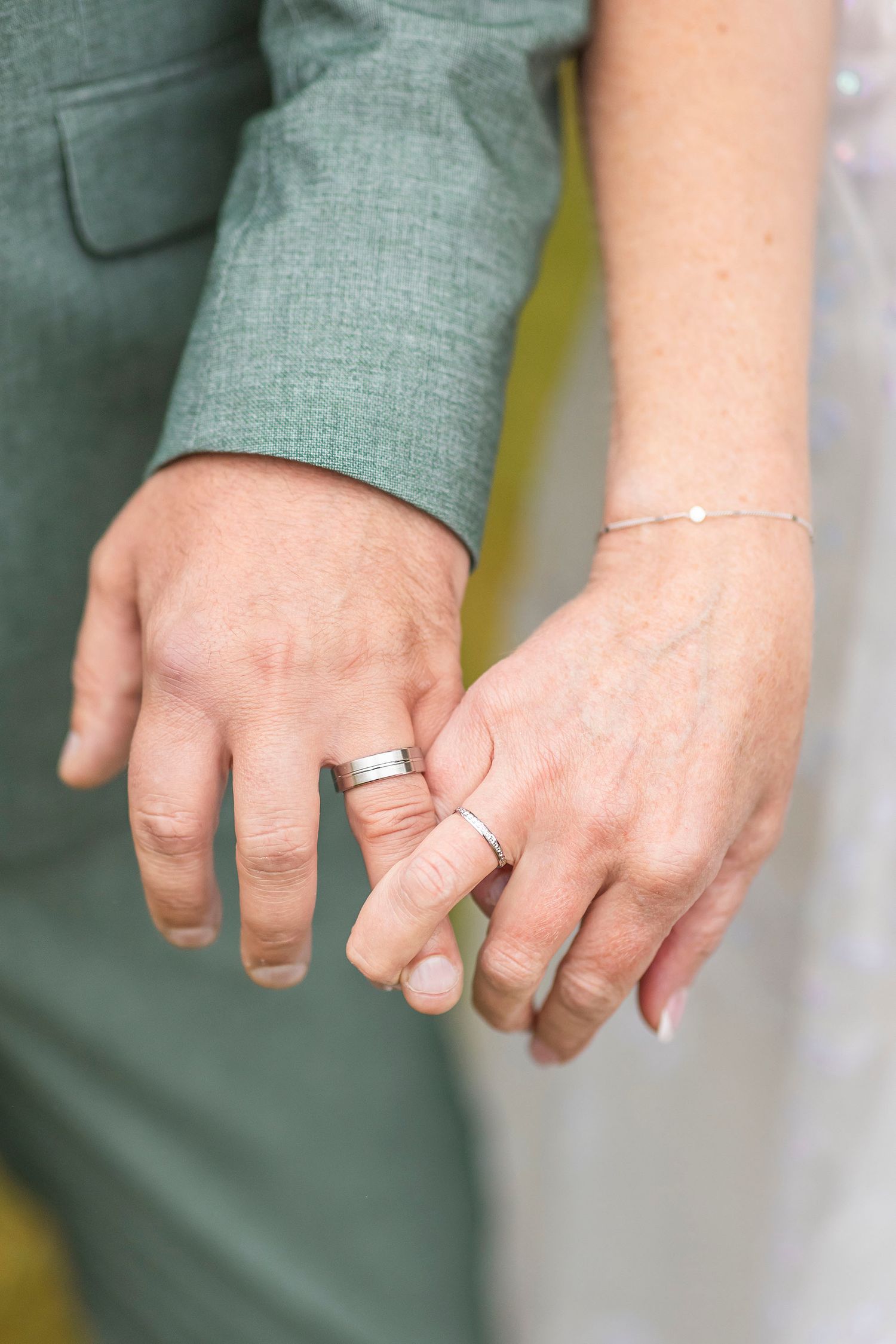 Close-up of hands showing delicate silver jewelry including a bracelet and rings against green fabric.