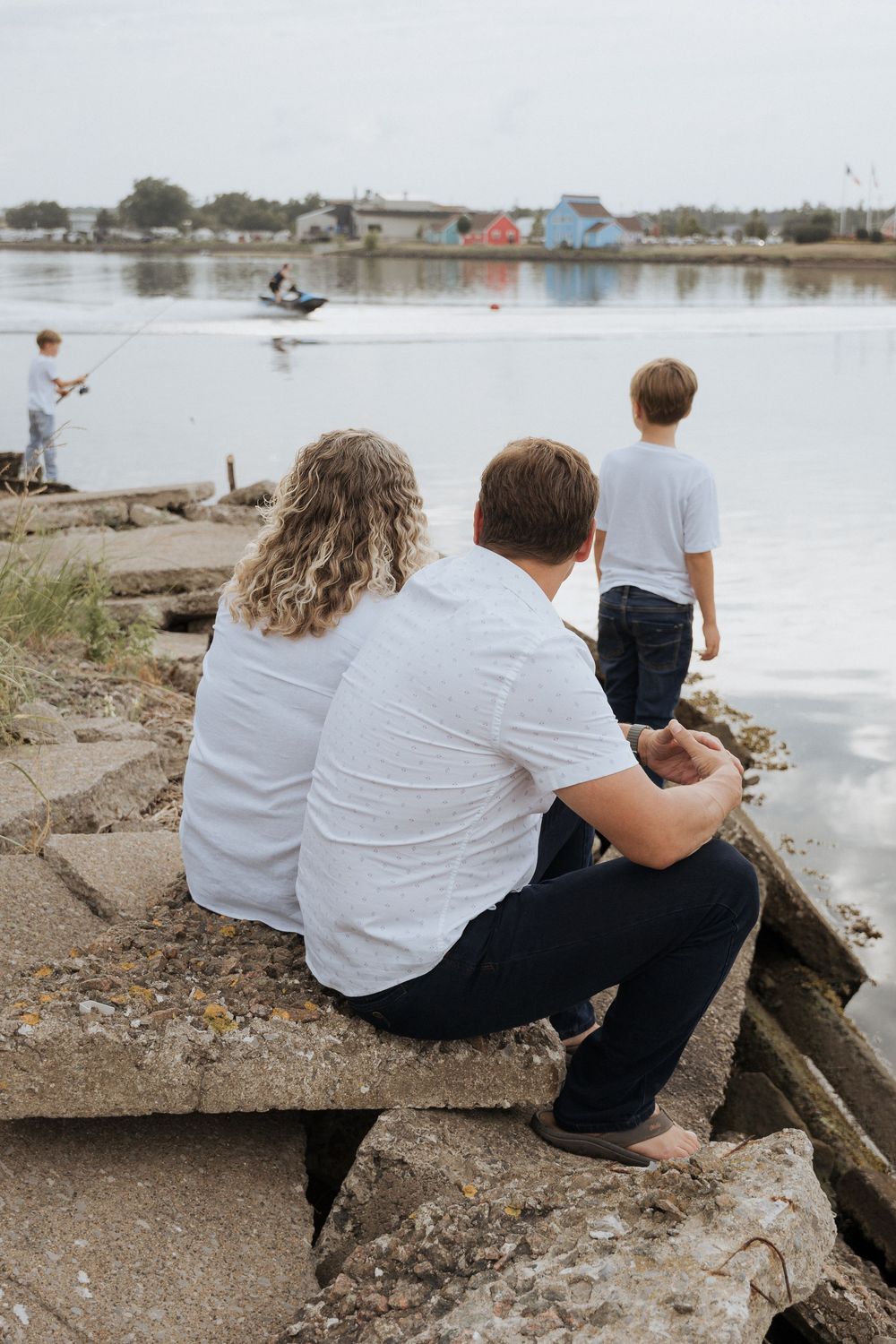 parents watching their son climb rocks at wharf marina during outdoor family portrait session, fun family portraits with no posing, candid
