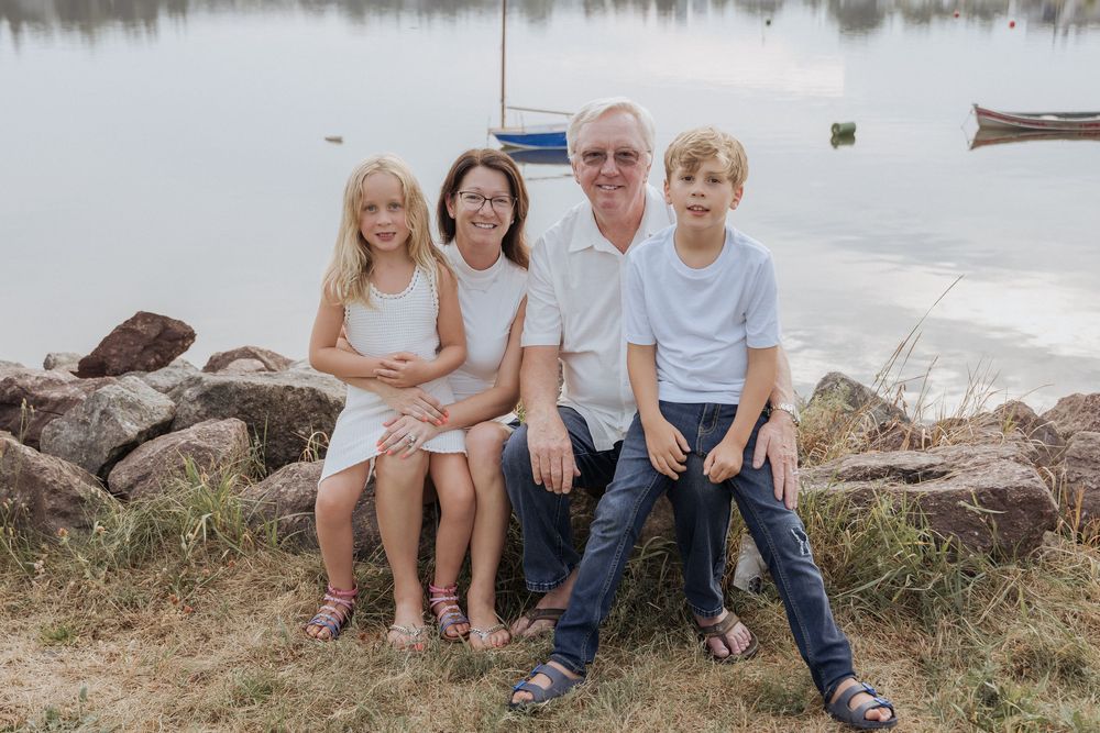 grandparents and grandchildren sitting by the water with boats reflecting in the background, Shediac photographer New Brunswick family