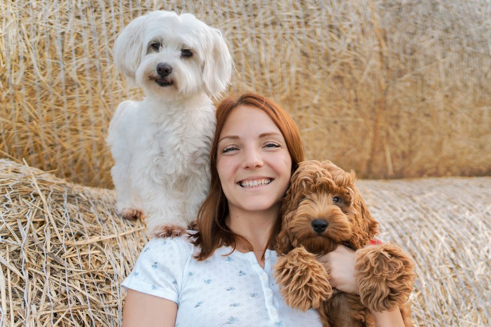 A woman poses outdoors with her two adorable dogs, a white Maltese and brown small dog Sydney photoshoot