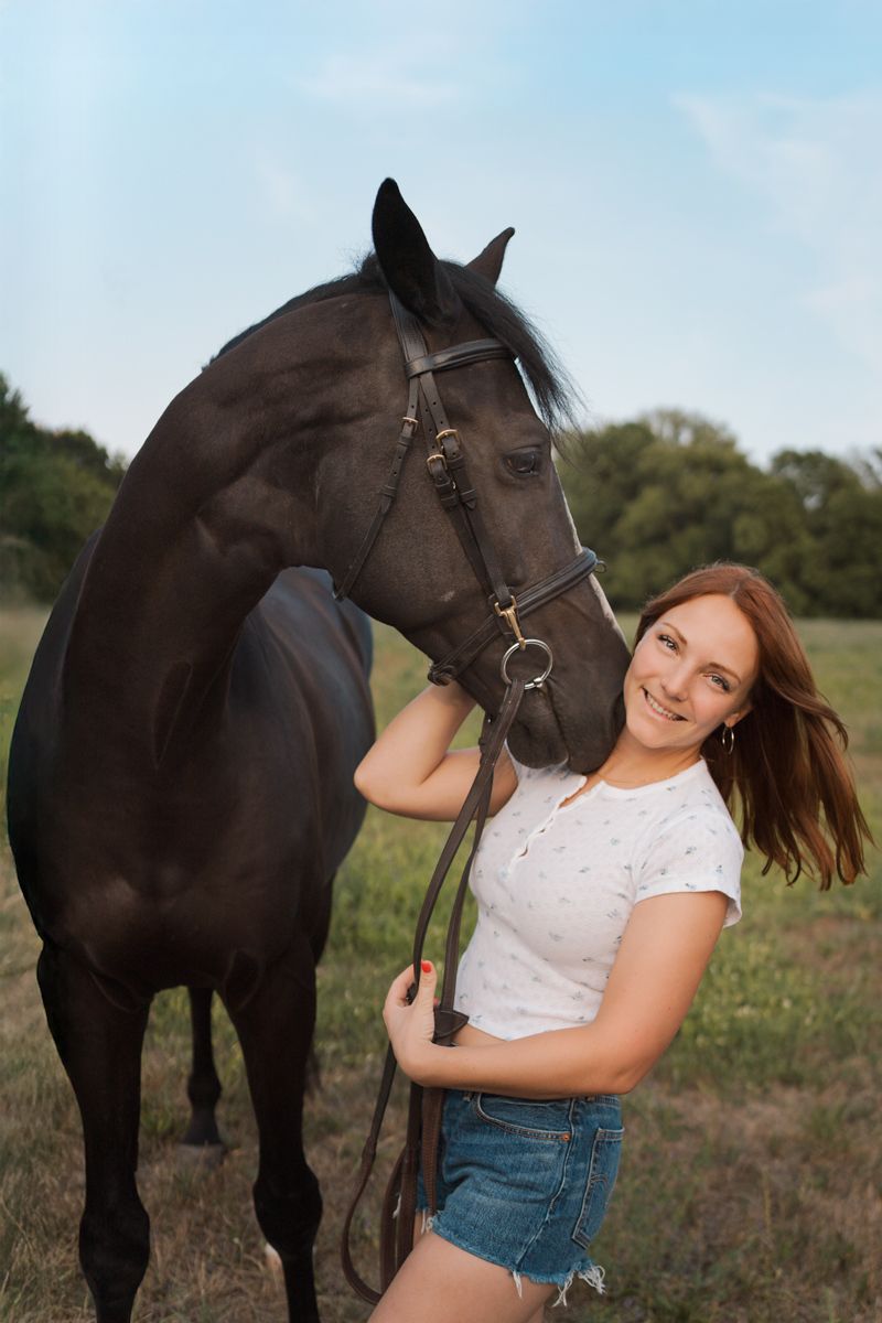 A young woman in denim shorts and white top poses playfully with her black horse in a summer field during a photoshoot sydney