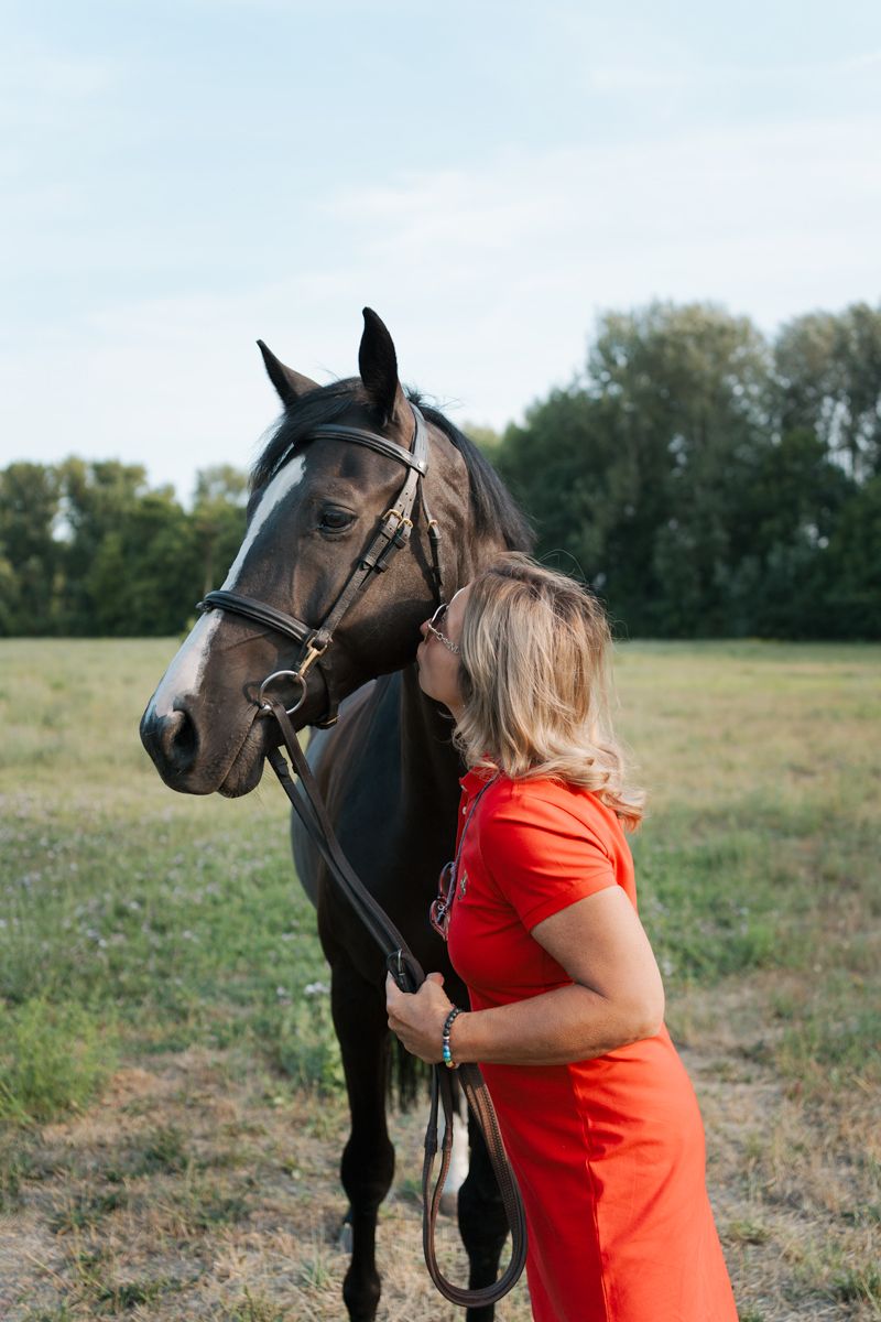 A person in a bright orange shirt hugs and bonds with a majestic black horse in a grassy field during a photoshoot in Sydney
