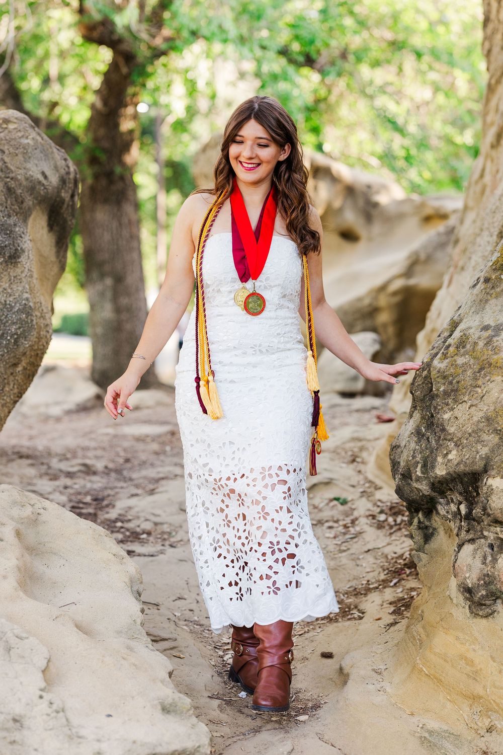 A white eyelet lace dress paired with brown boots and colorful sash photographed in a natural outdoor setting.