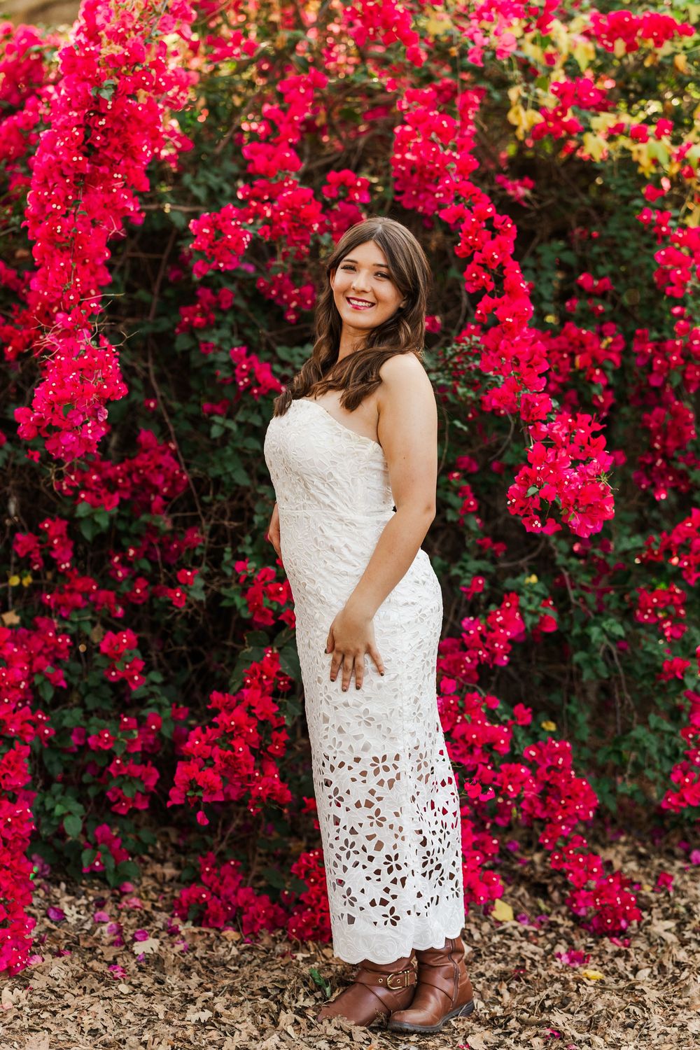 A white lace dress stands out against vibrant red bougainvillea flowers in full bloom.