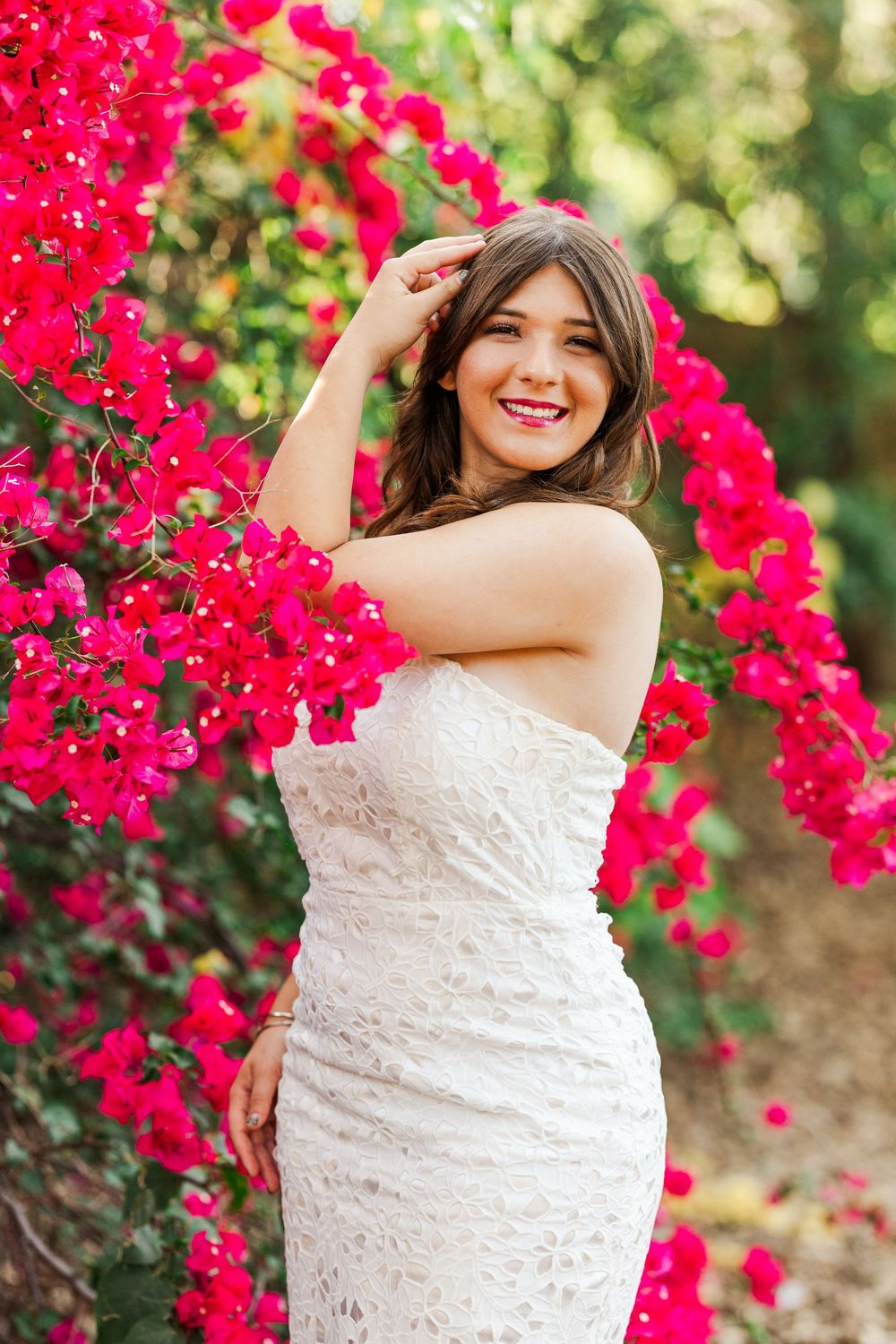 White lace dress contrasts beautifully with vibrant red bougainvillea flowers in an outdoor garden setting.