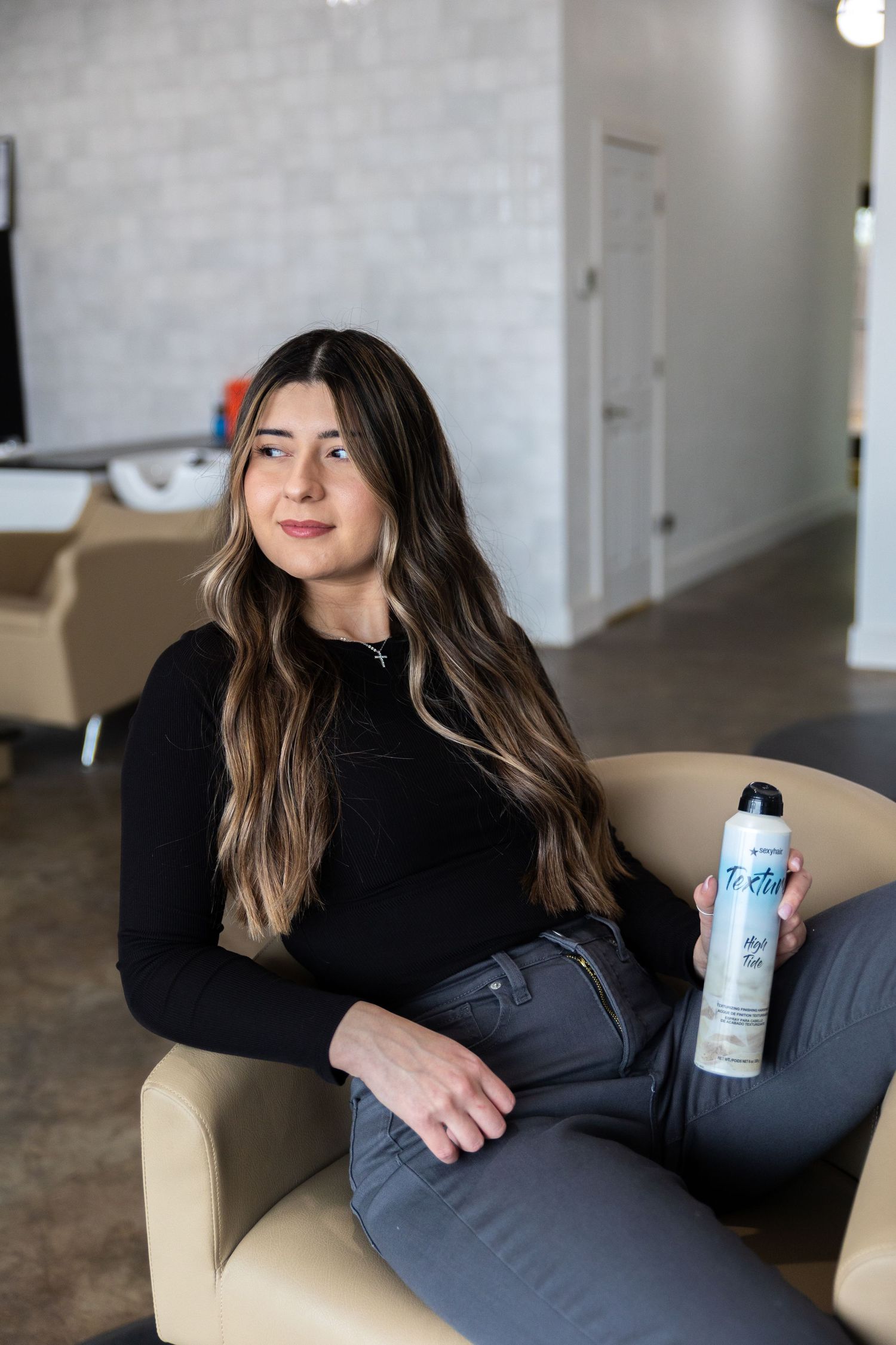 A person in a black sweater relaxes on a beige chair while holding a white beverage can.
