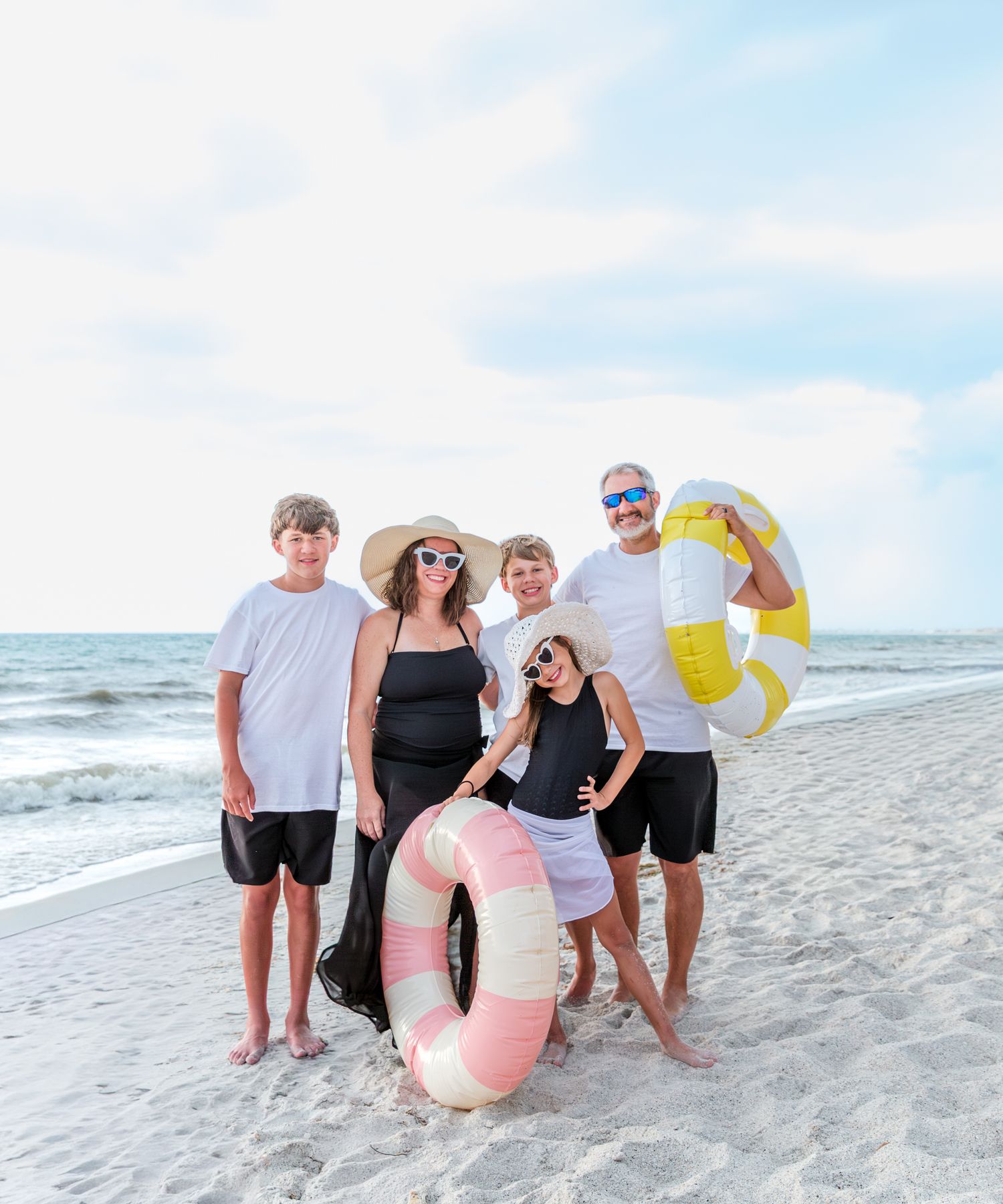 Family of five posing on sandy beach holding colorful inflatable pool floats.