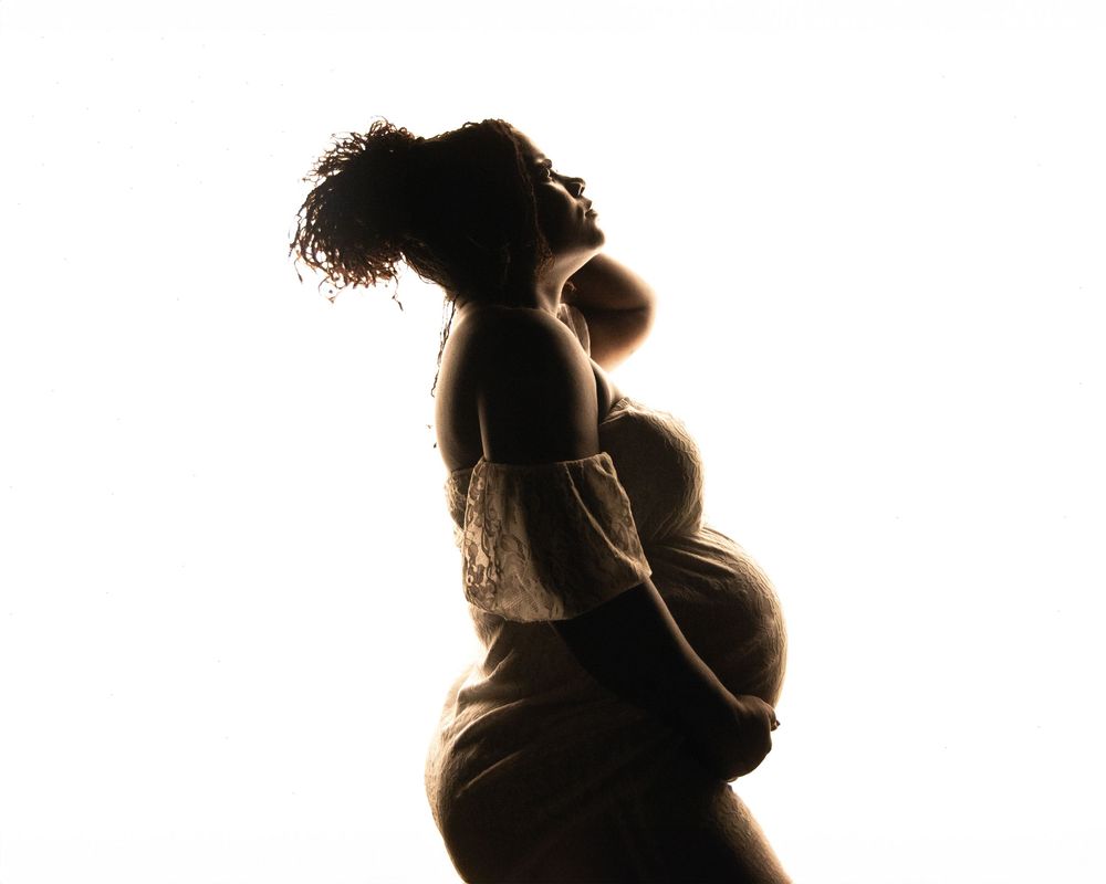 Silhouetted maternity progression photos showing pregnancy stages from early to late term against white background.