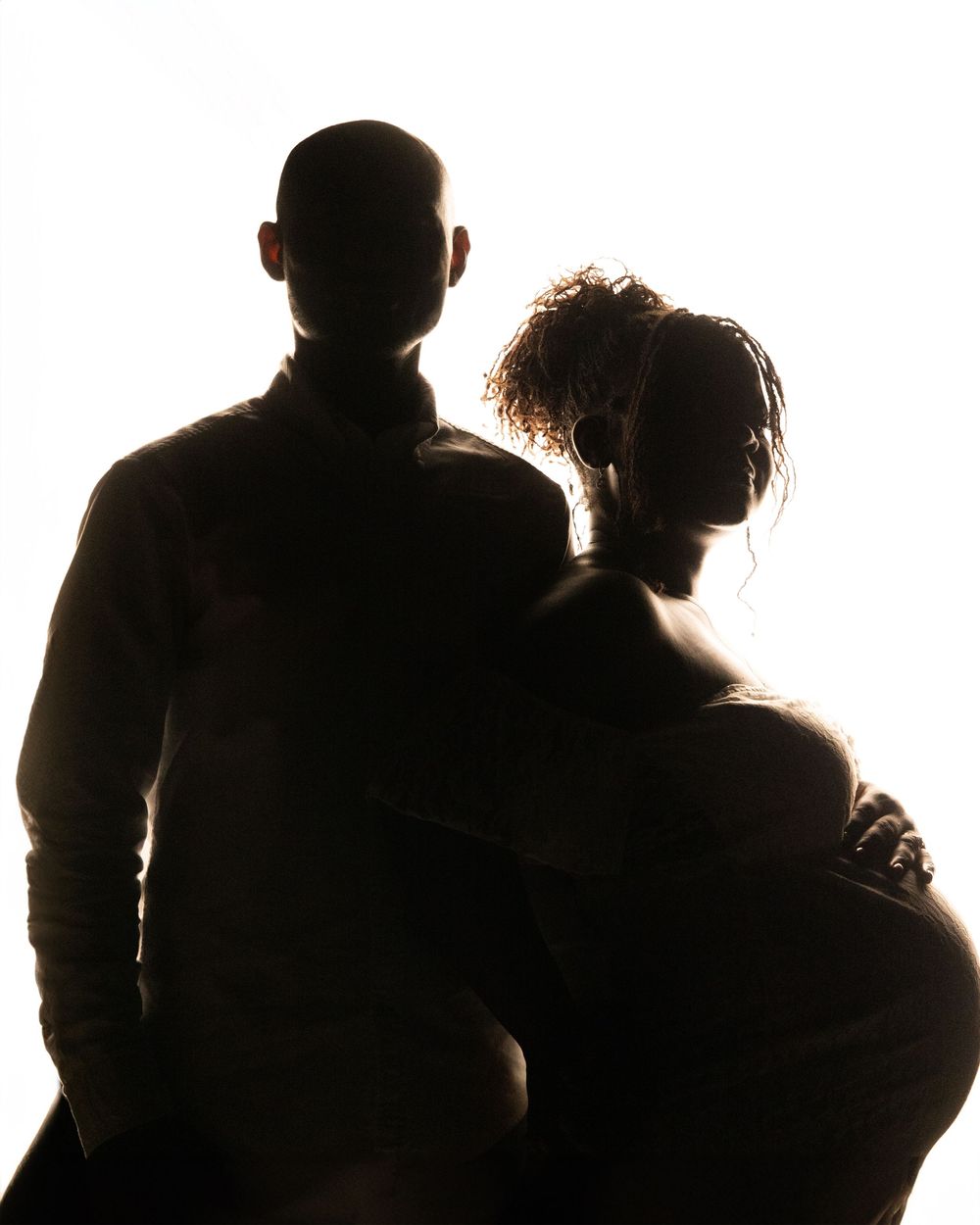 Silhouettes of a group of people standing together against a bright background.