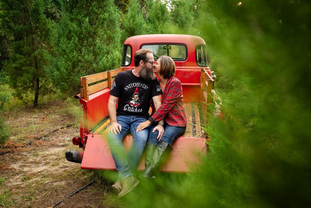 A couple sits together in a vintage red truck surrounded by lush green forest scenery during a romantic photoshoot.