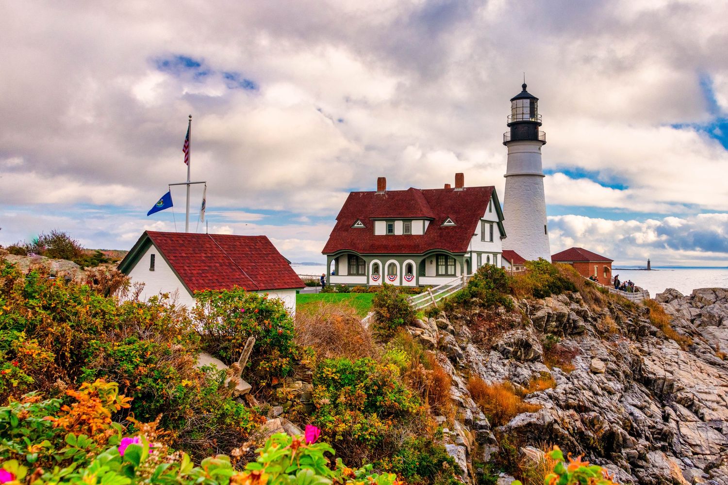 A series of coastal lighthouses with rocky shores and vibrant fall foliage against dramatic cloudy skies.