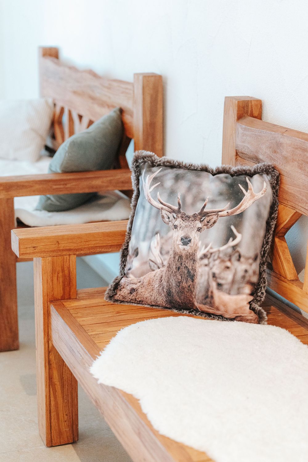 Modern wooden outdoor bench with decorative throw pillows and cushions against a light-colored wall.