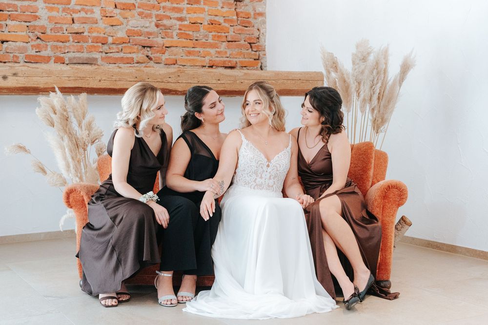 A group in formal attire sits on an orange velvet couch against a brick wall with pampas grass decor.