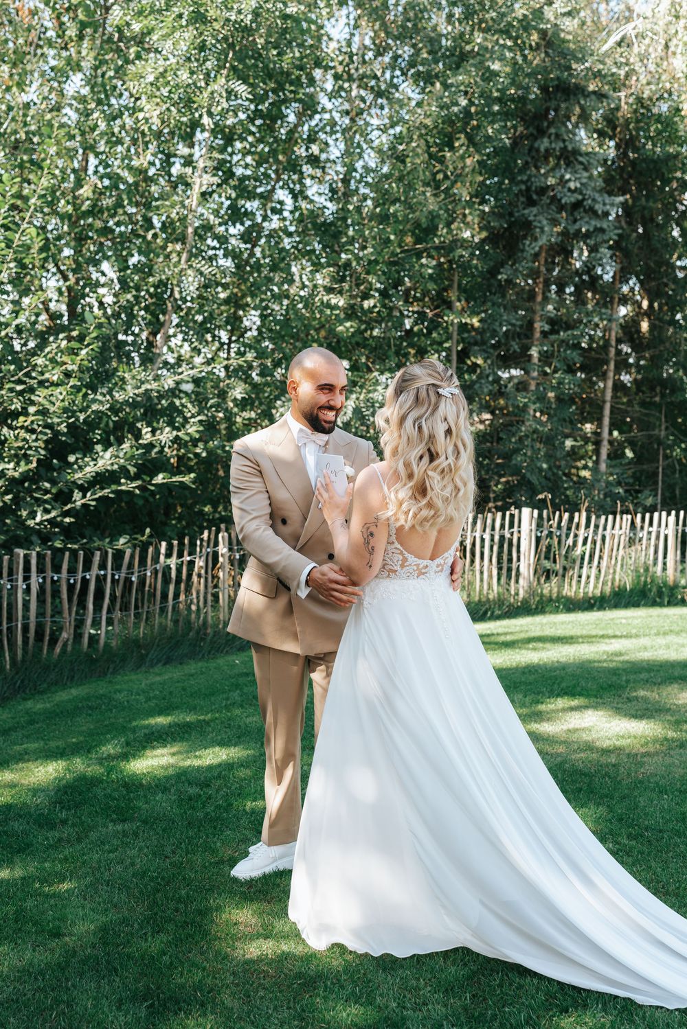 A joyful couple dances together on a sunny lawn surrounded by trees while the bride's white dress flows elegantly.