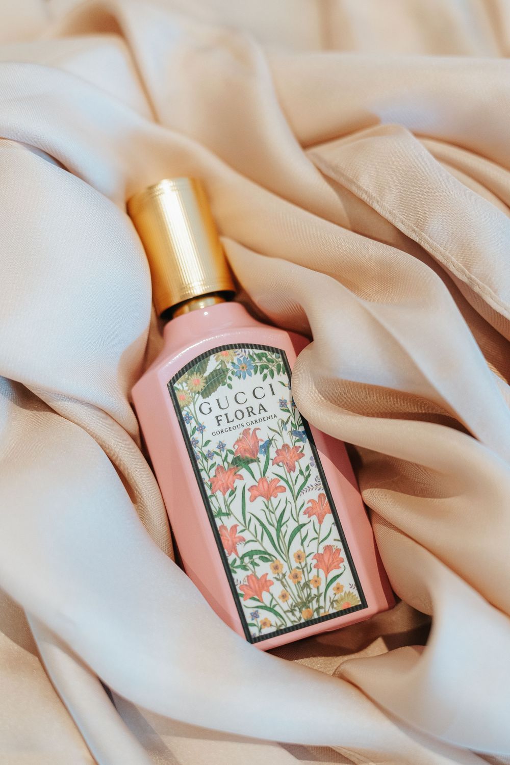 Luxury Gucci Flora perfume bottle with floral pattern design rests on soft beige silk fabric in multiple angles.