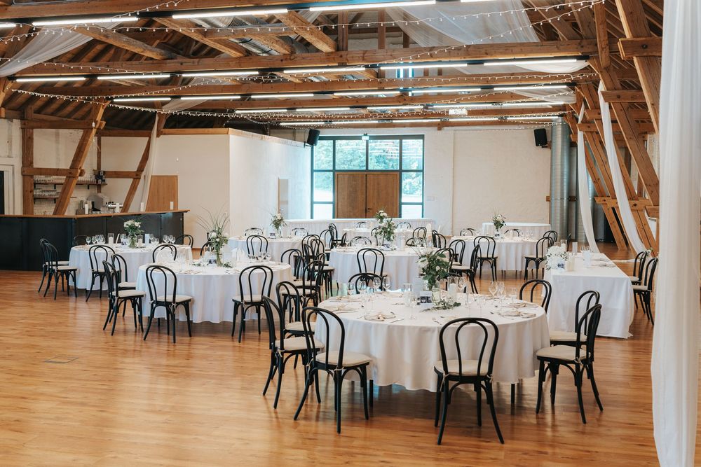 Rustic barn venue with exposed wooden beams and white round tables set up for an elegant wedding reception.