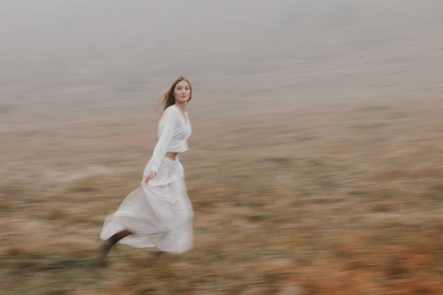Jeune femme courant dans un champ brumeux lors d'une séance photo lifestyle en pleine nature.