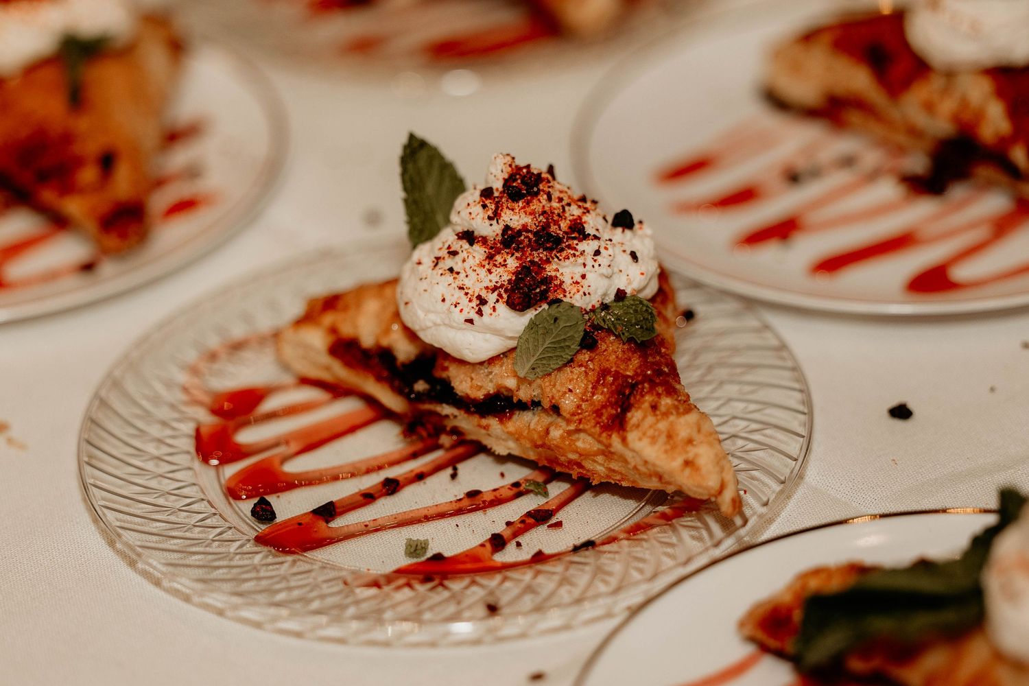 Elegant plated dessert with chocolate drizzle and red garnish on a clear glass plate.