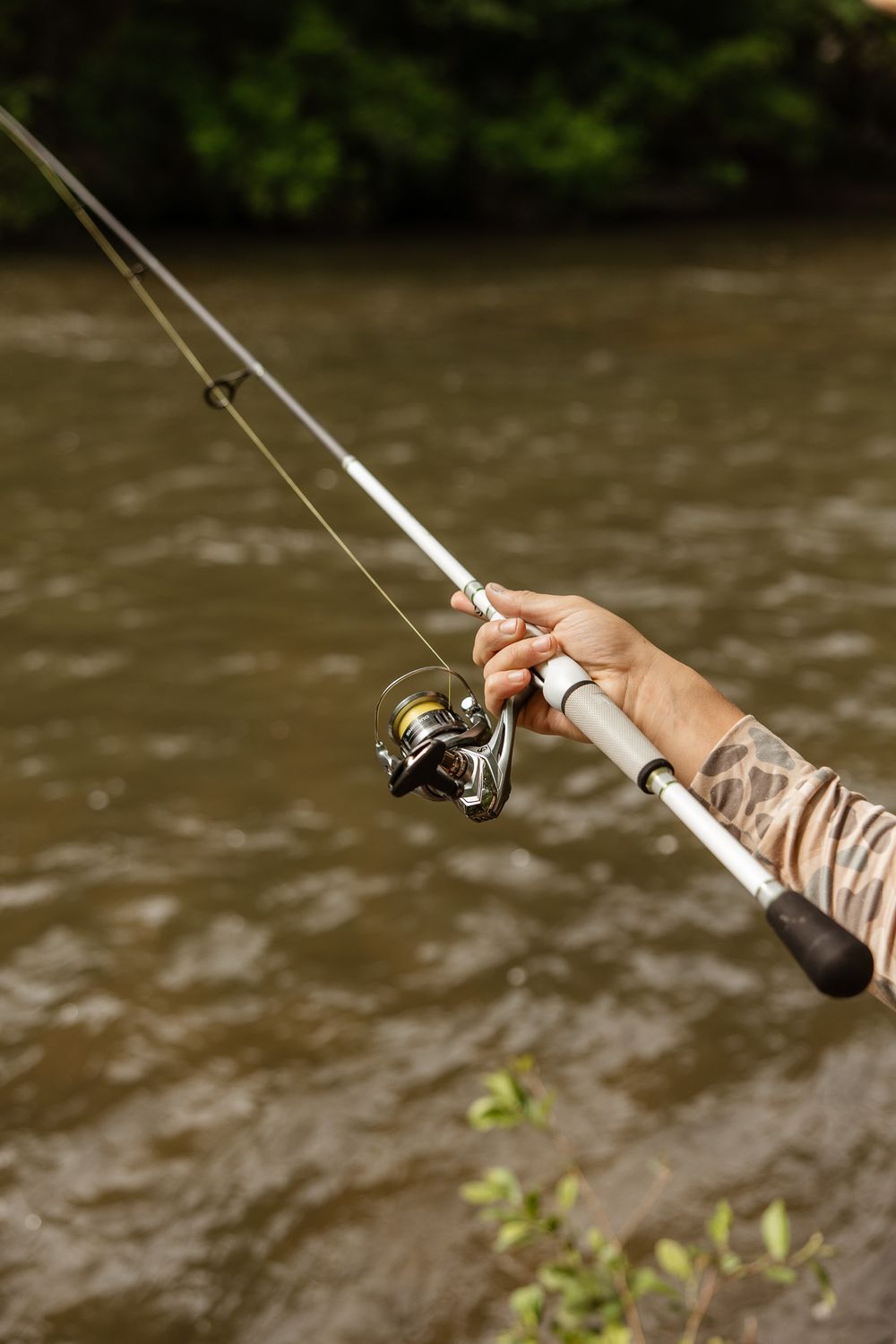 Close-up sequence of hands holding fishing rod and reel against blurred river background.