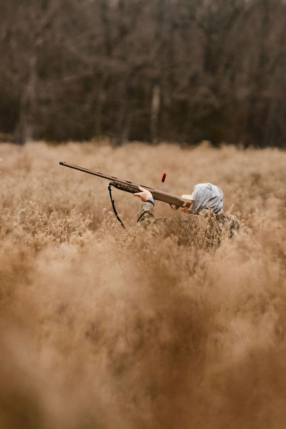 A dog emerges through tall brown grass while carrying a hunting decoy in its mouth during field training.