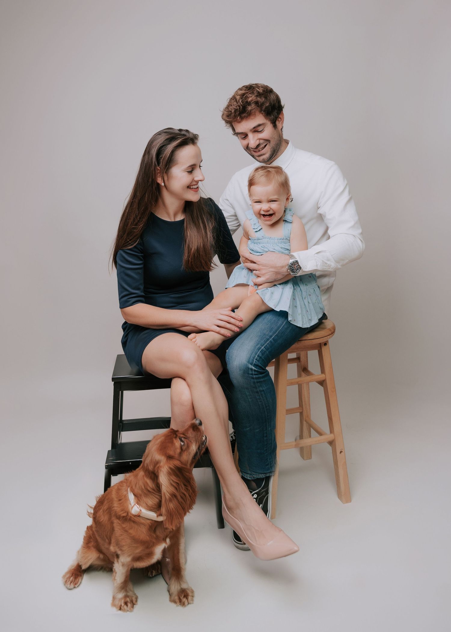 Family and golden retriever dog pose together for casual studio portraits against a light gray backdrop.