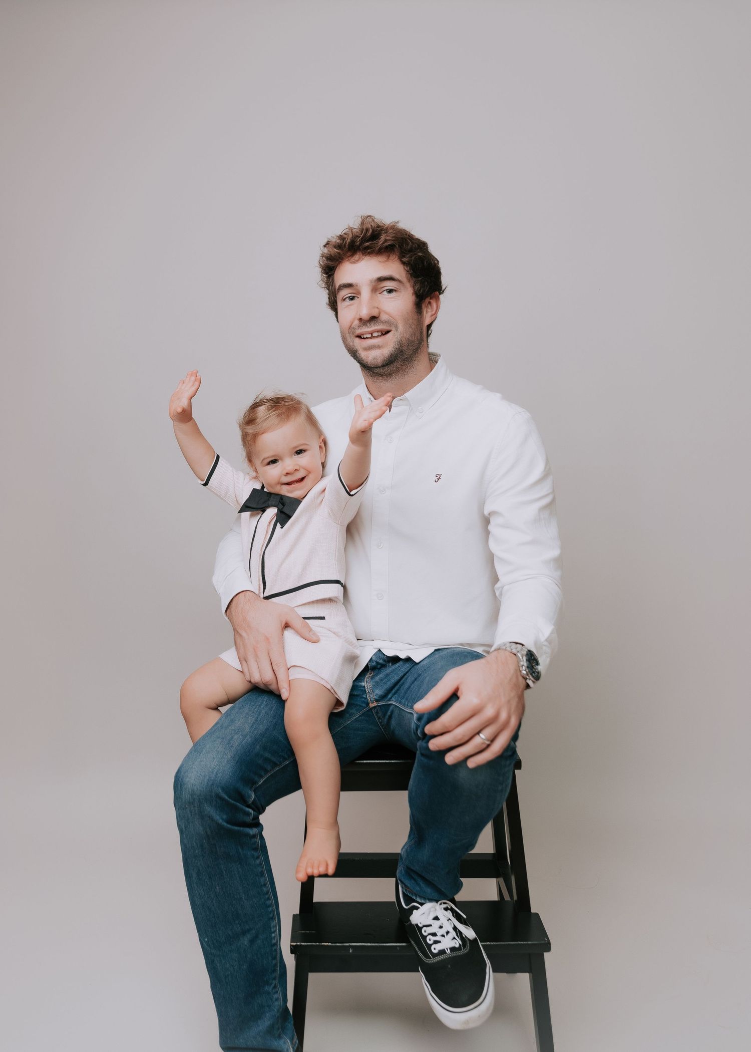 A sequence of candid studio portraits showing playful interactions between two people on a simple chair against gray backdrop.
