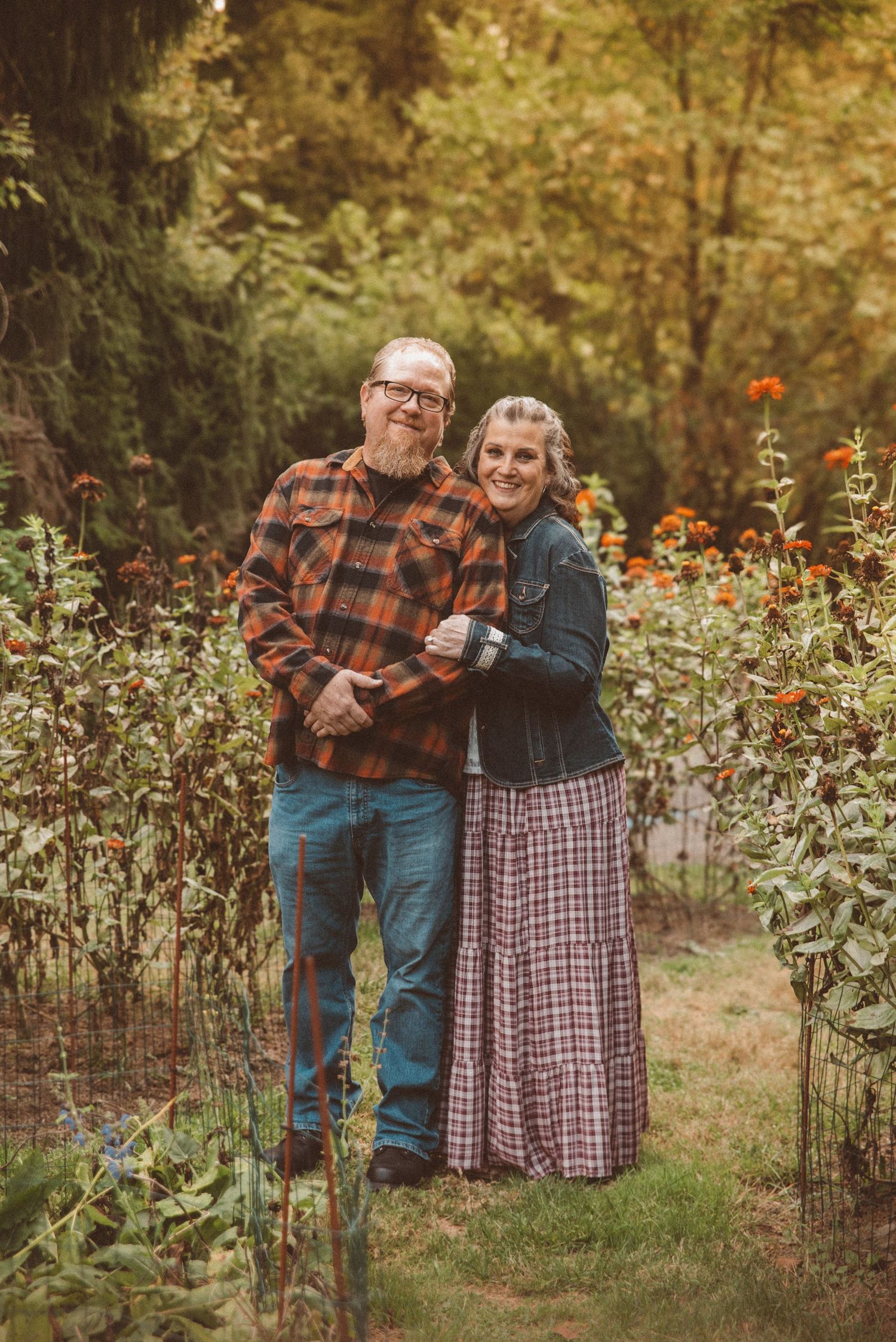 A couple posing together in the middle of a garden of tall orange flowers.