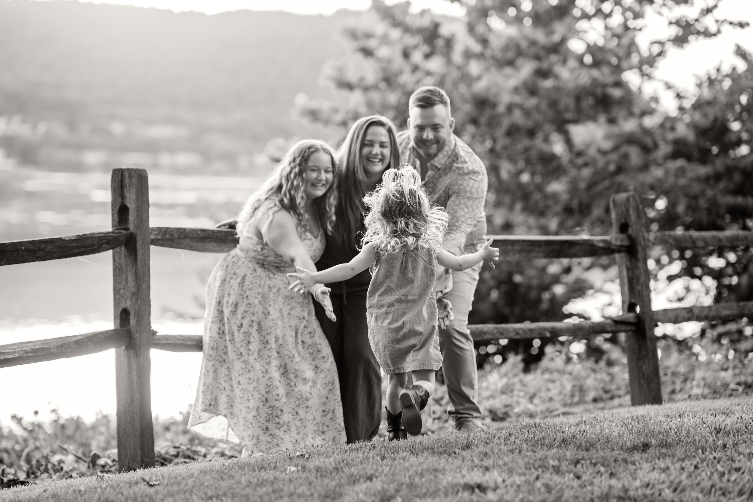 A family plays together in a grassy meadow with wooden fence posts at sunset, creating a heartwarming silhouette.