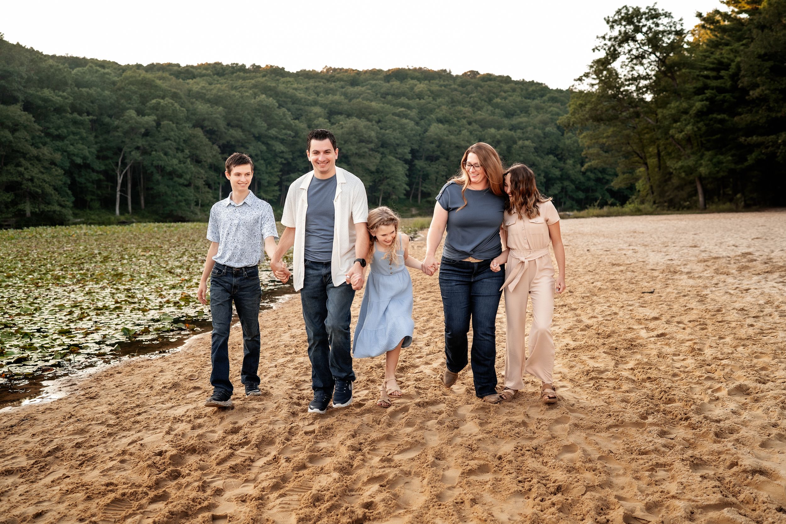 Family members walk together on a dirt path through scenic rural farmland at sunset.