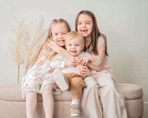 A series of sweet candid moments between siblings sitting together on a beige couch, showing laughter and affection.
