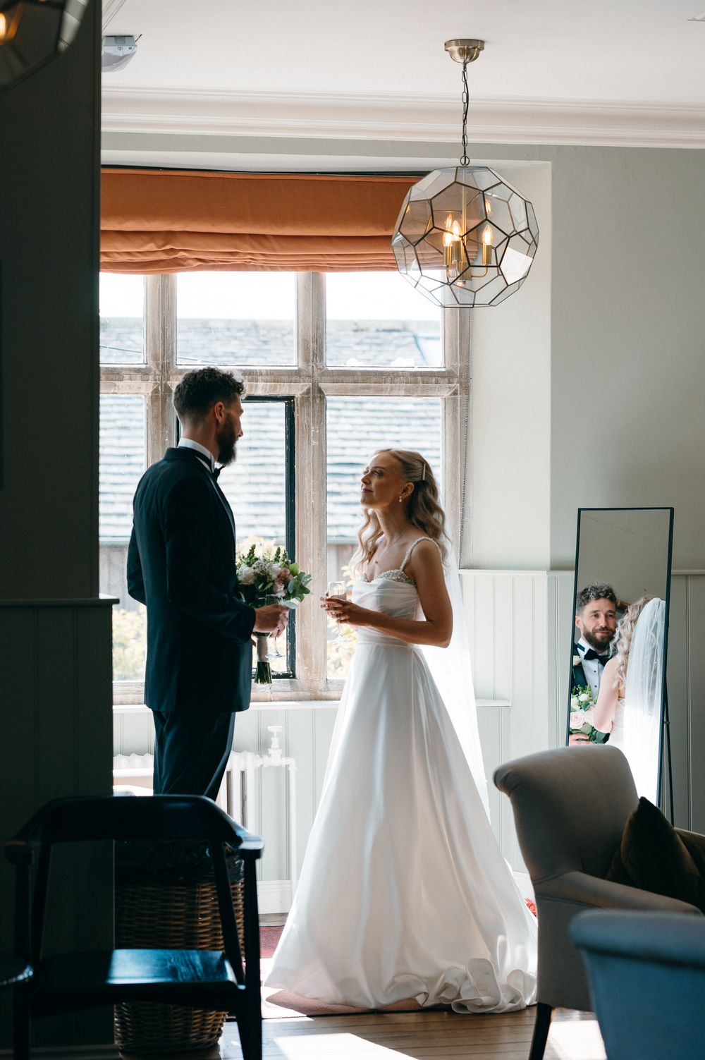 A couple in formal wedding attire share a special moment together while holding drinks in a bright interior space.
