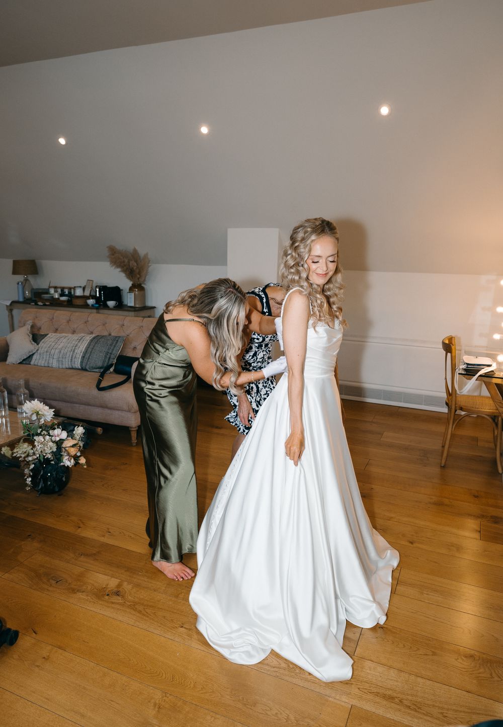 A sequence of photos showing someone being helped into a white wedding dress on a hardwood floor.