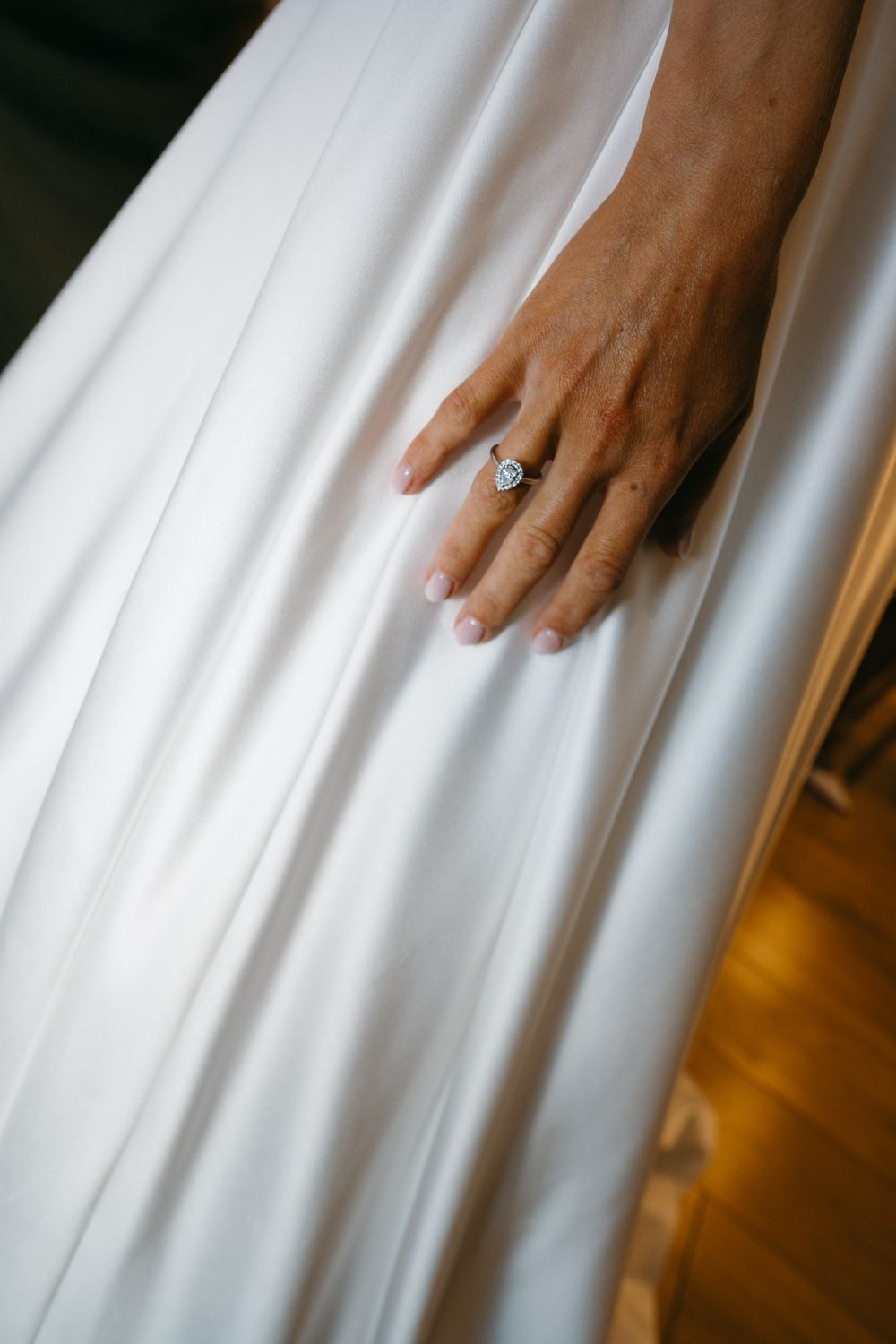 A diamond engagement ring sparkles on a hand resting against flowing white wedding dress fabric.
