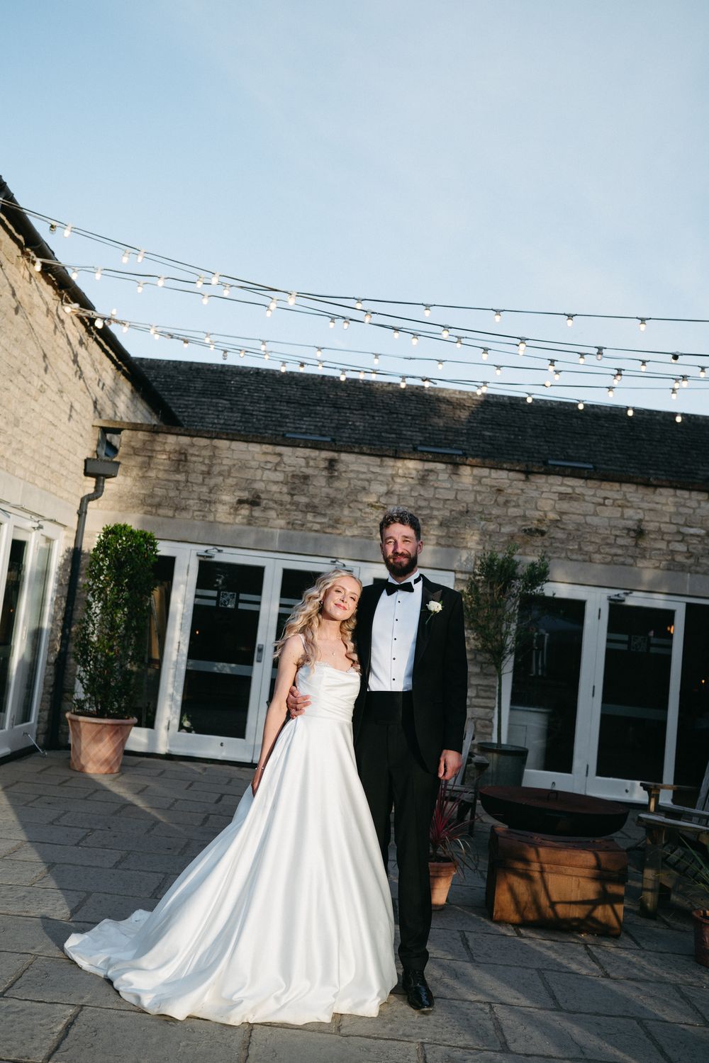 A couple dances together on an outdoor patio with string lights overhead during their wedding reception.