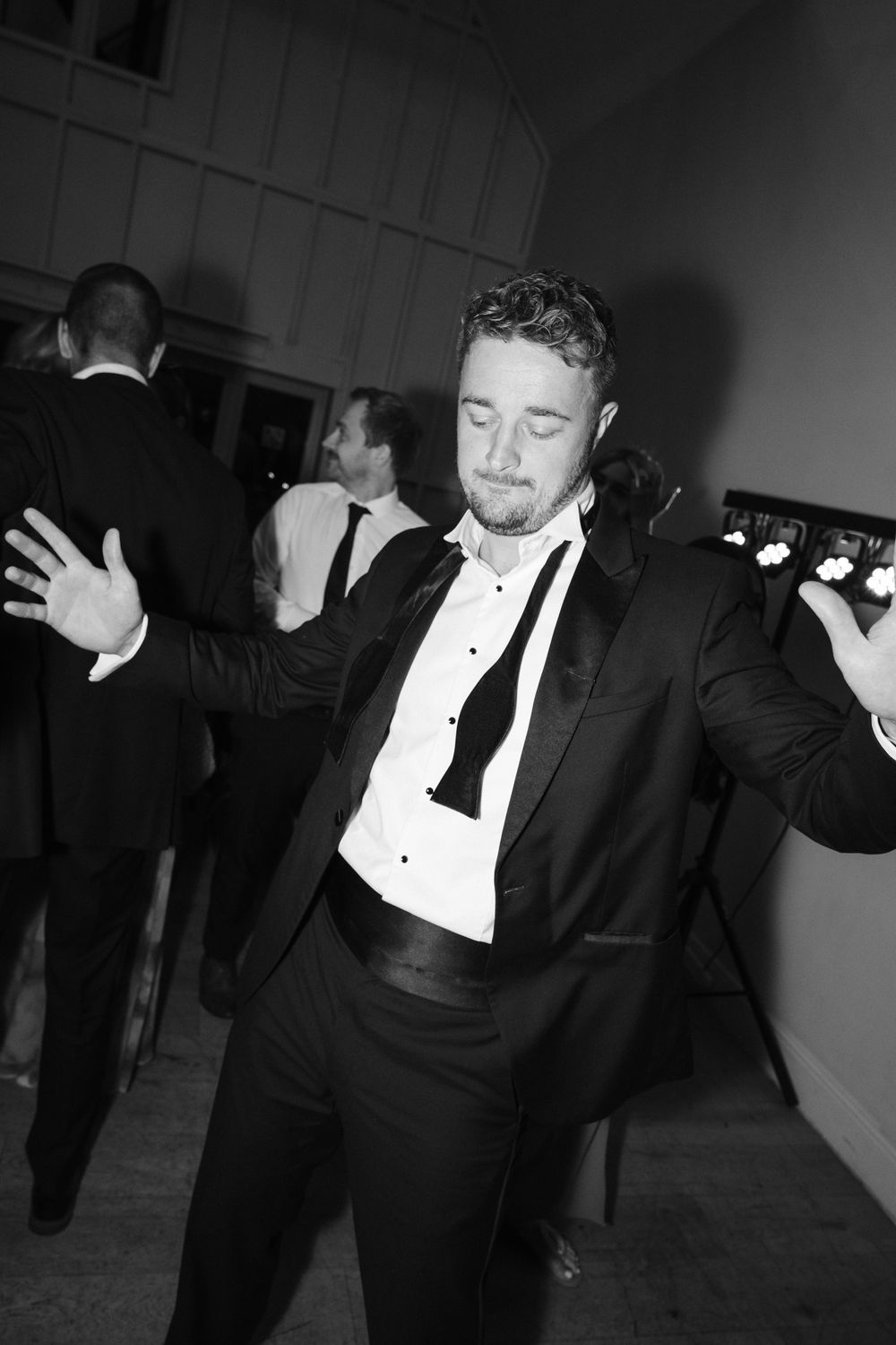 Black and white photo series showing someone in a tuxedo dancing and moving energetically at a formal event.
