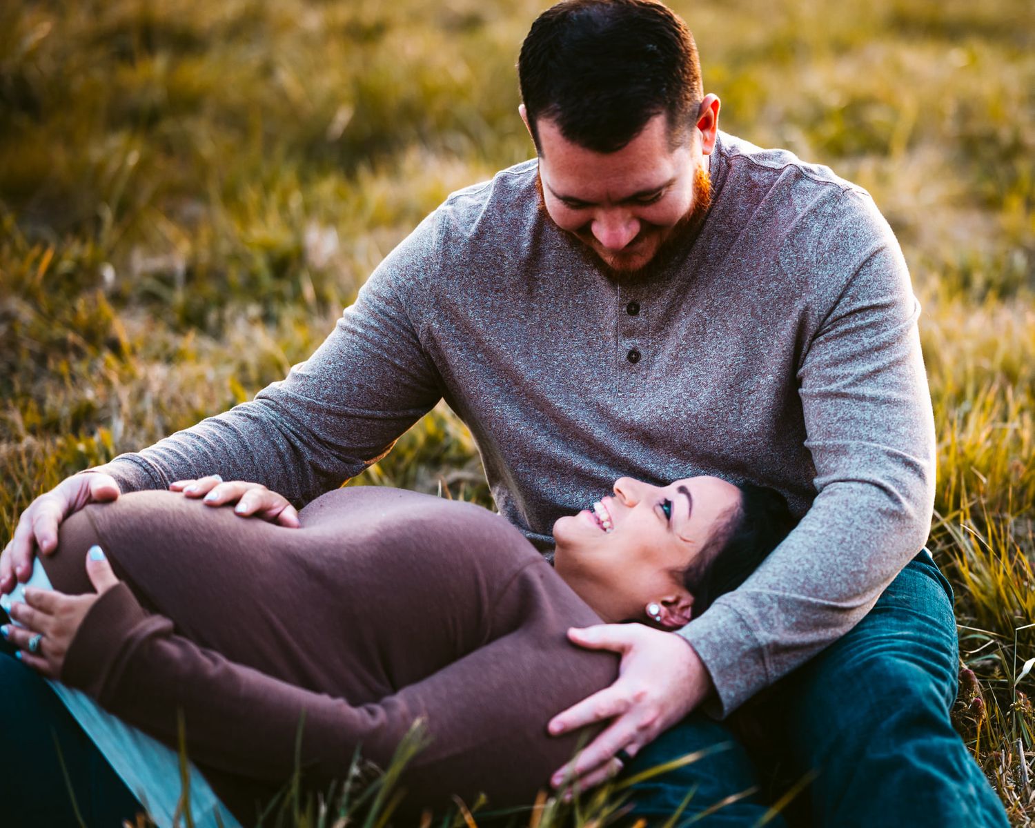 Couple lying on grass during golden hour outdoor photoshoot with romantic poses.
