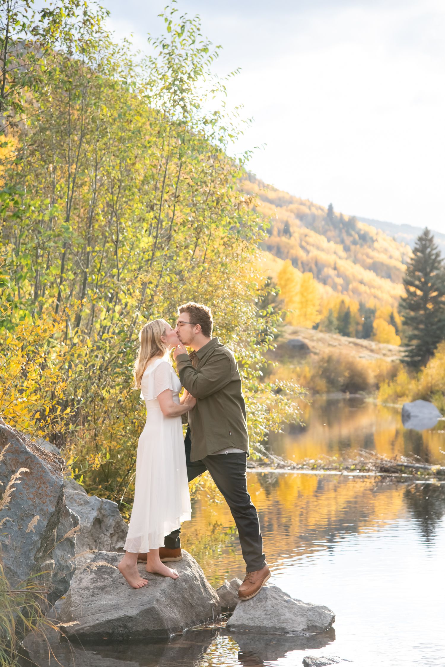 cute couple with stylish outfits standing on a rock in the creek with fall colors on the mountains behind them in Vail Colorado engagement